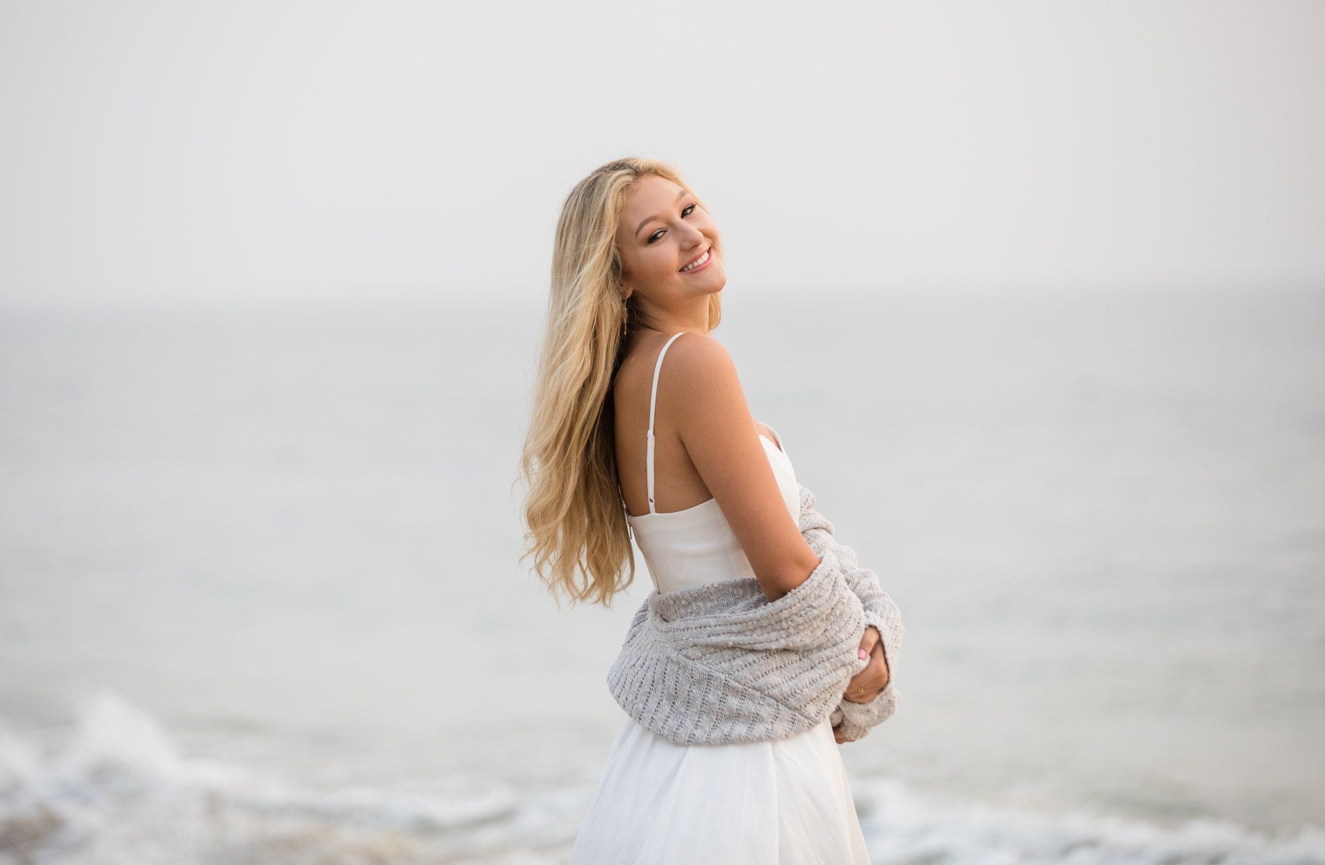A woman in a white dress is standing on the beach.