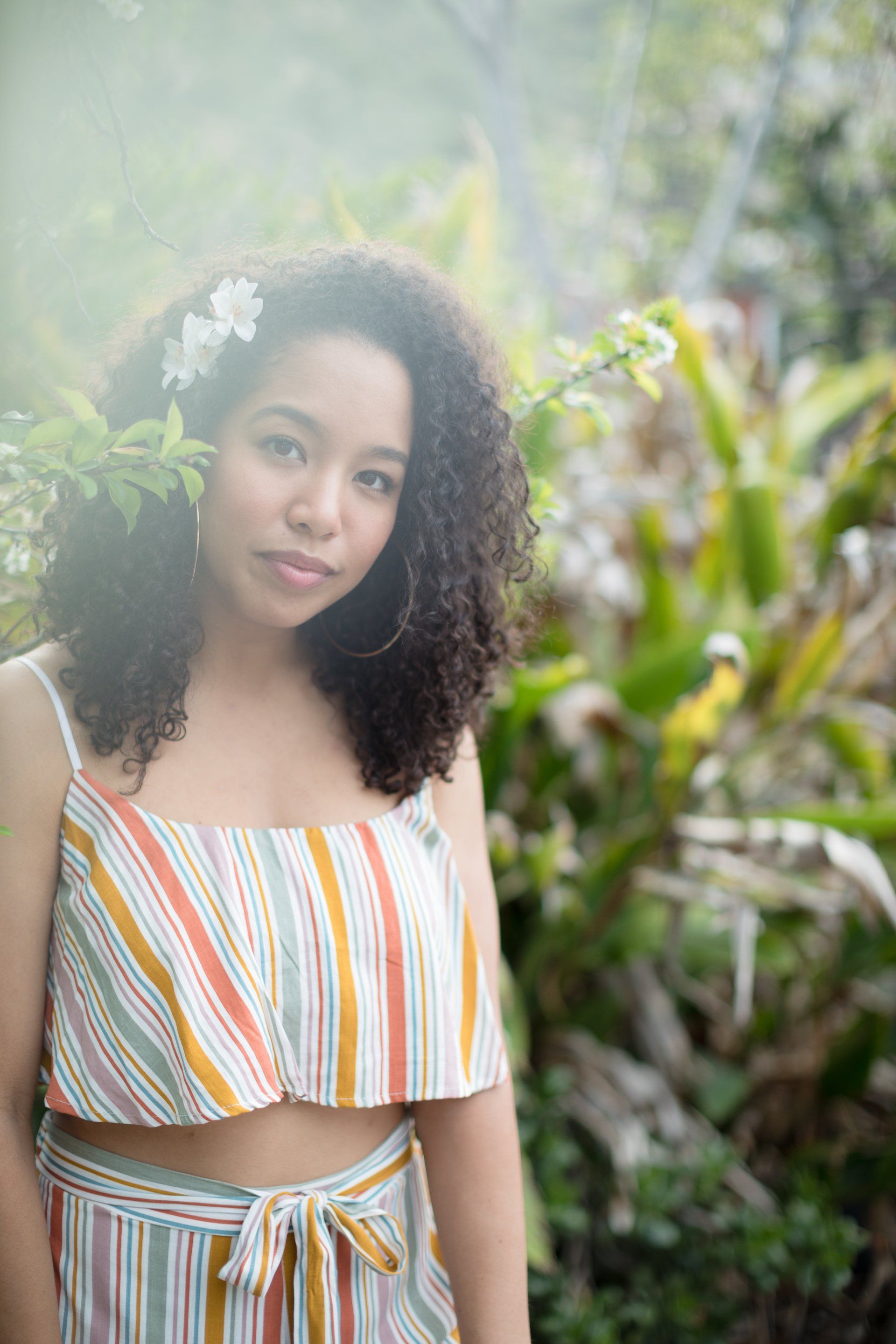 A young woman with curly hair is wearing a striped crop top and skirt.
