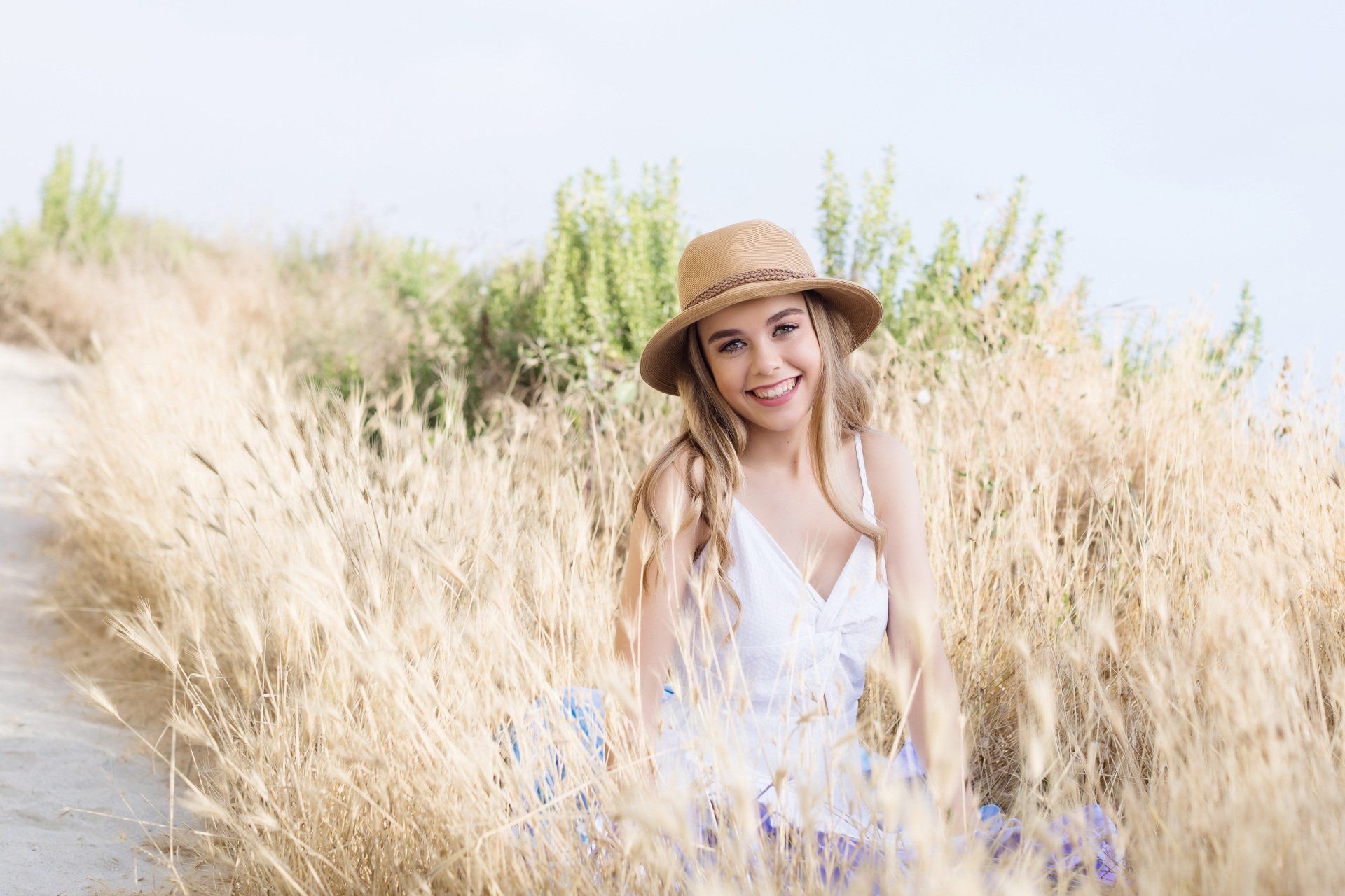 A woman in a hat is sitting in a field of tall grass.