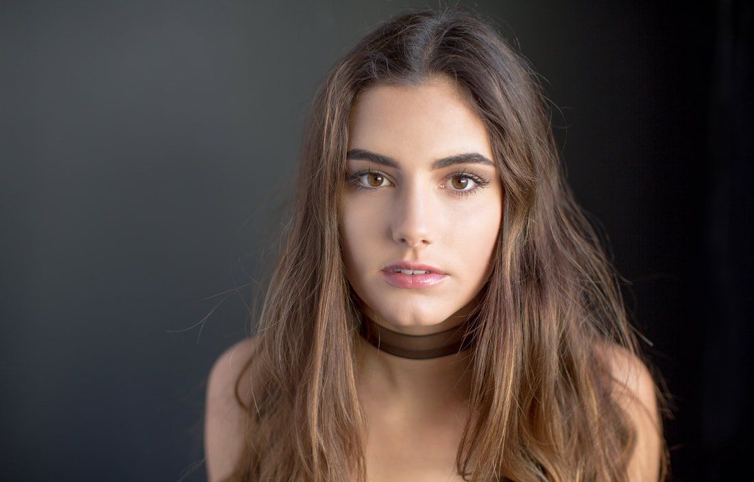 A woman with long hair is wearing a choker and looking at the camera.