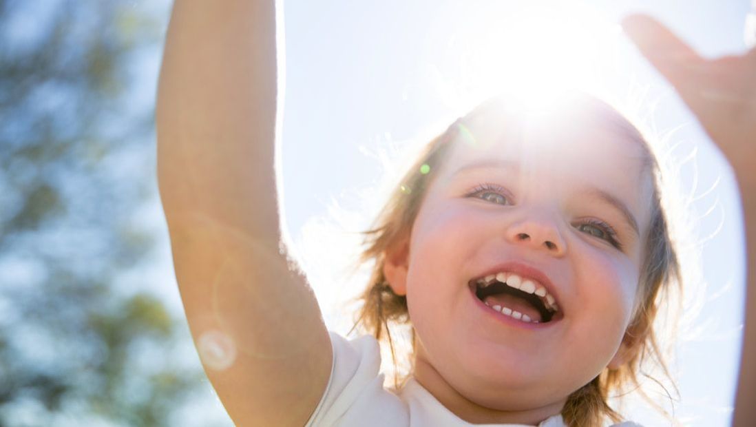 A little girl is holding her hands up in the air and smiling.