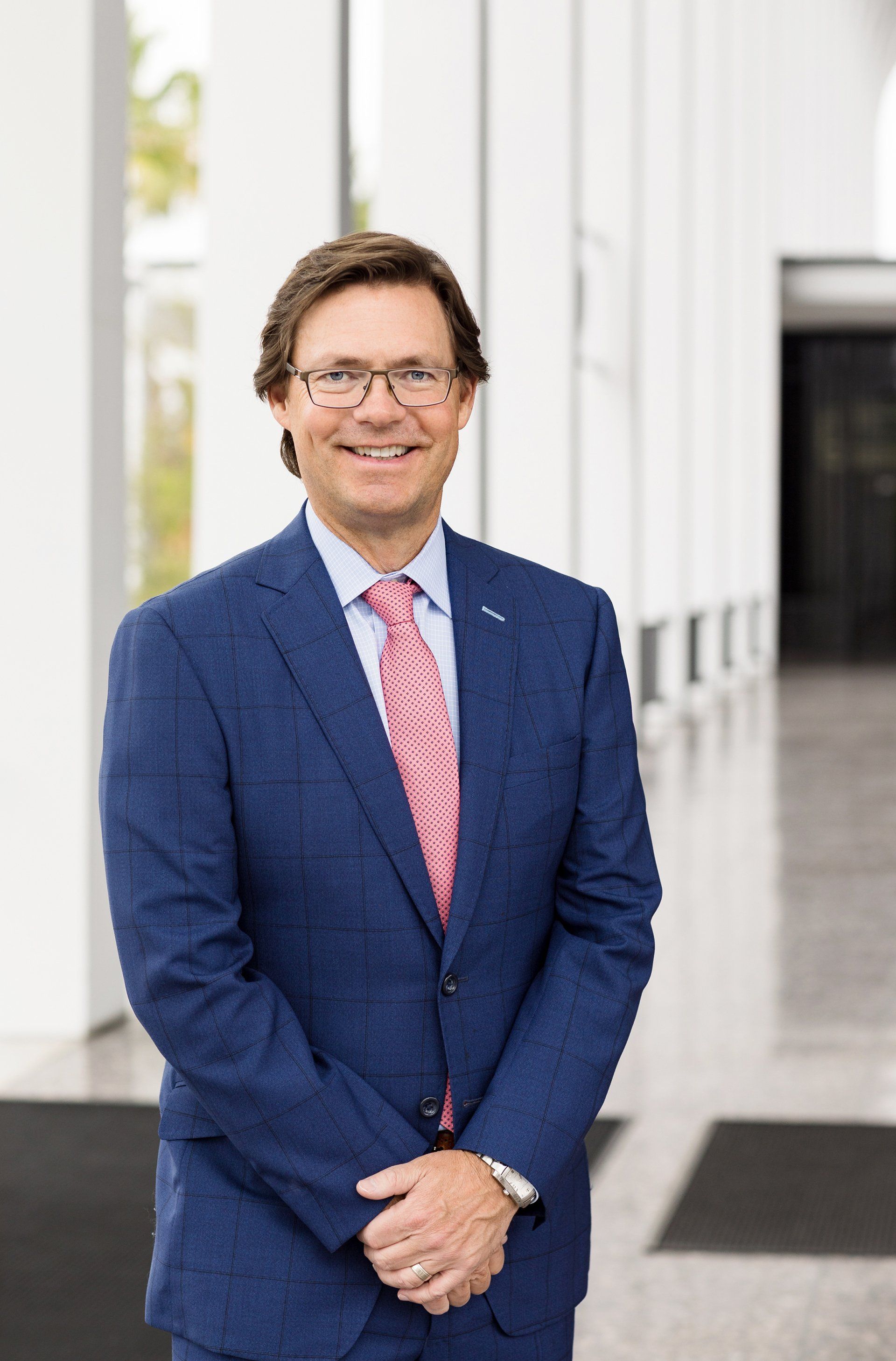 A man in a blue suit and pink tie is smiling for the camera.