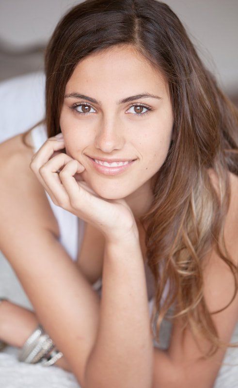 A woman is laying on a bed with her hand on her chin.