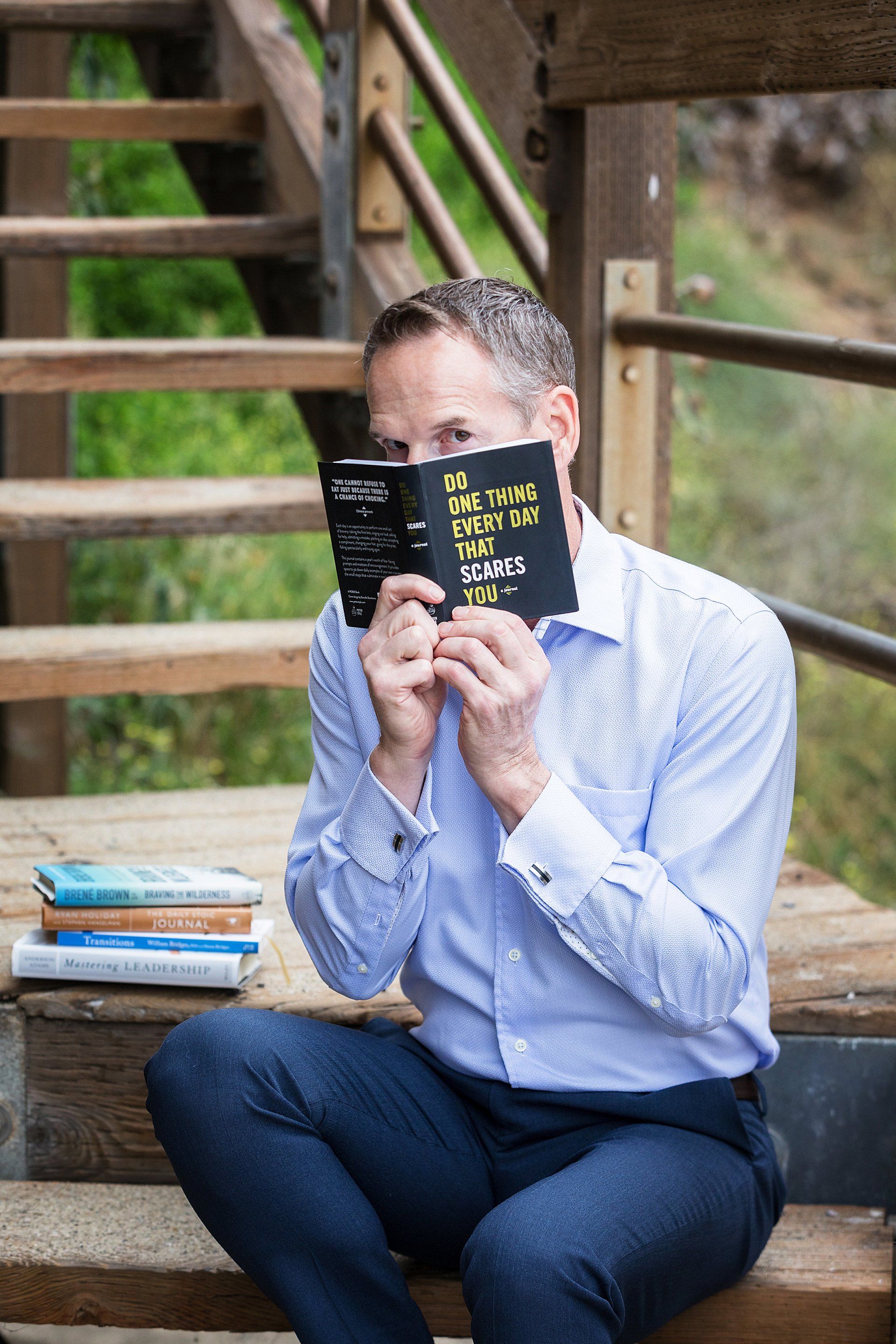 A man is sitting on a set of stairs holding a book in front of his face.