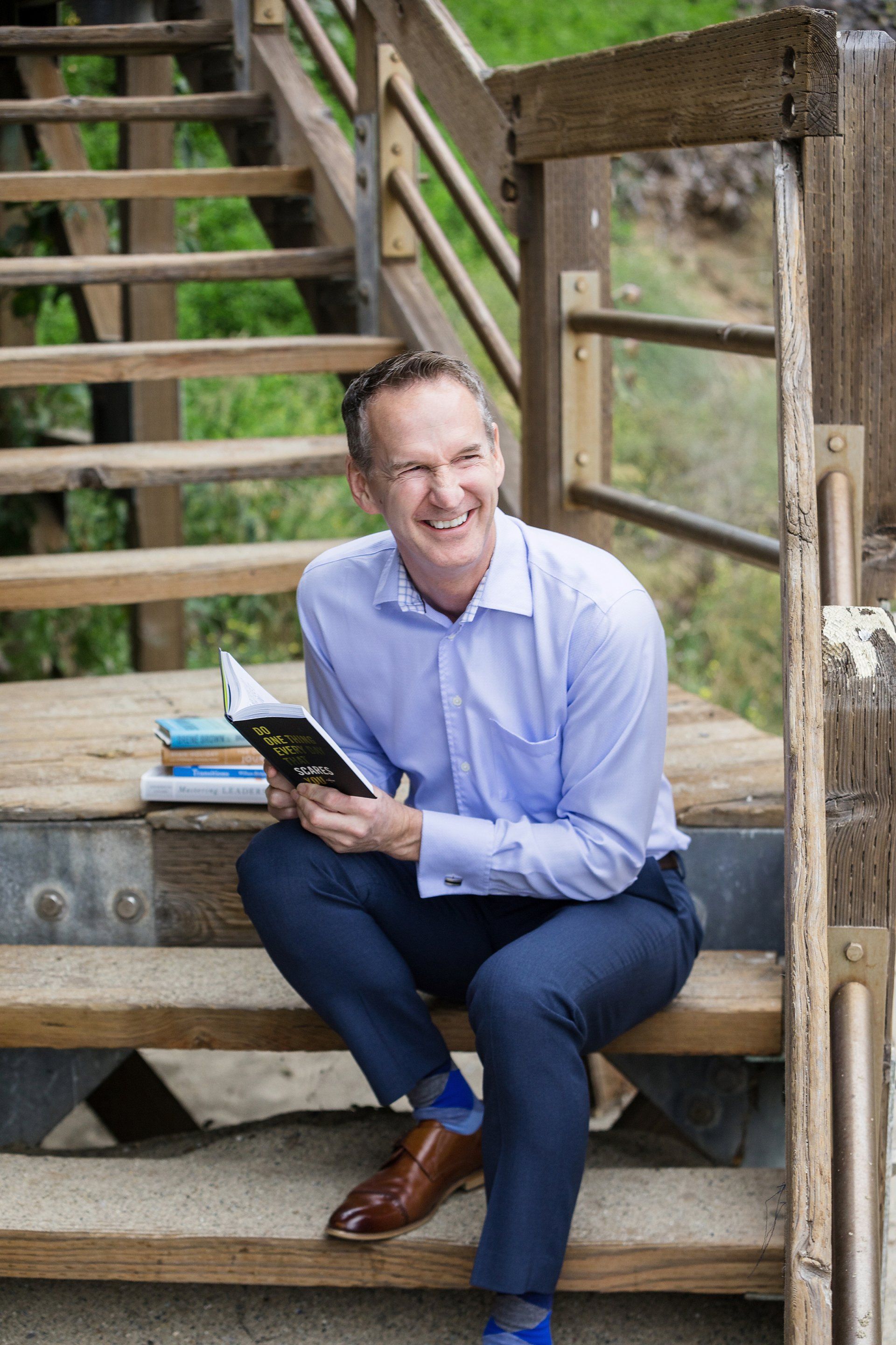 A man is sitting on a set of wooden stairs holding a book.