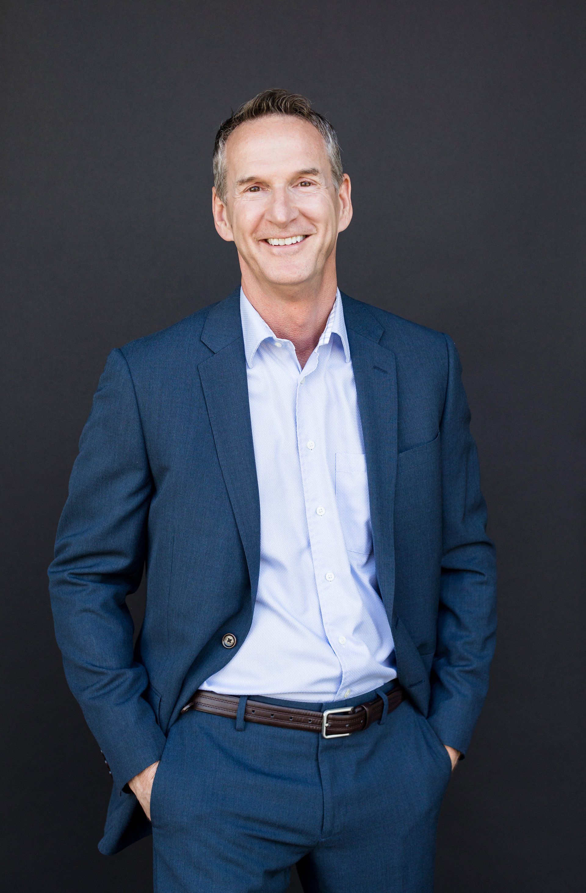 A man in a blue suit and white shirt is standing with his hands in his pockets.
