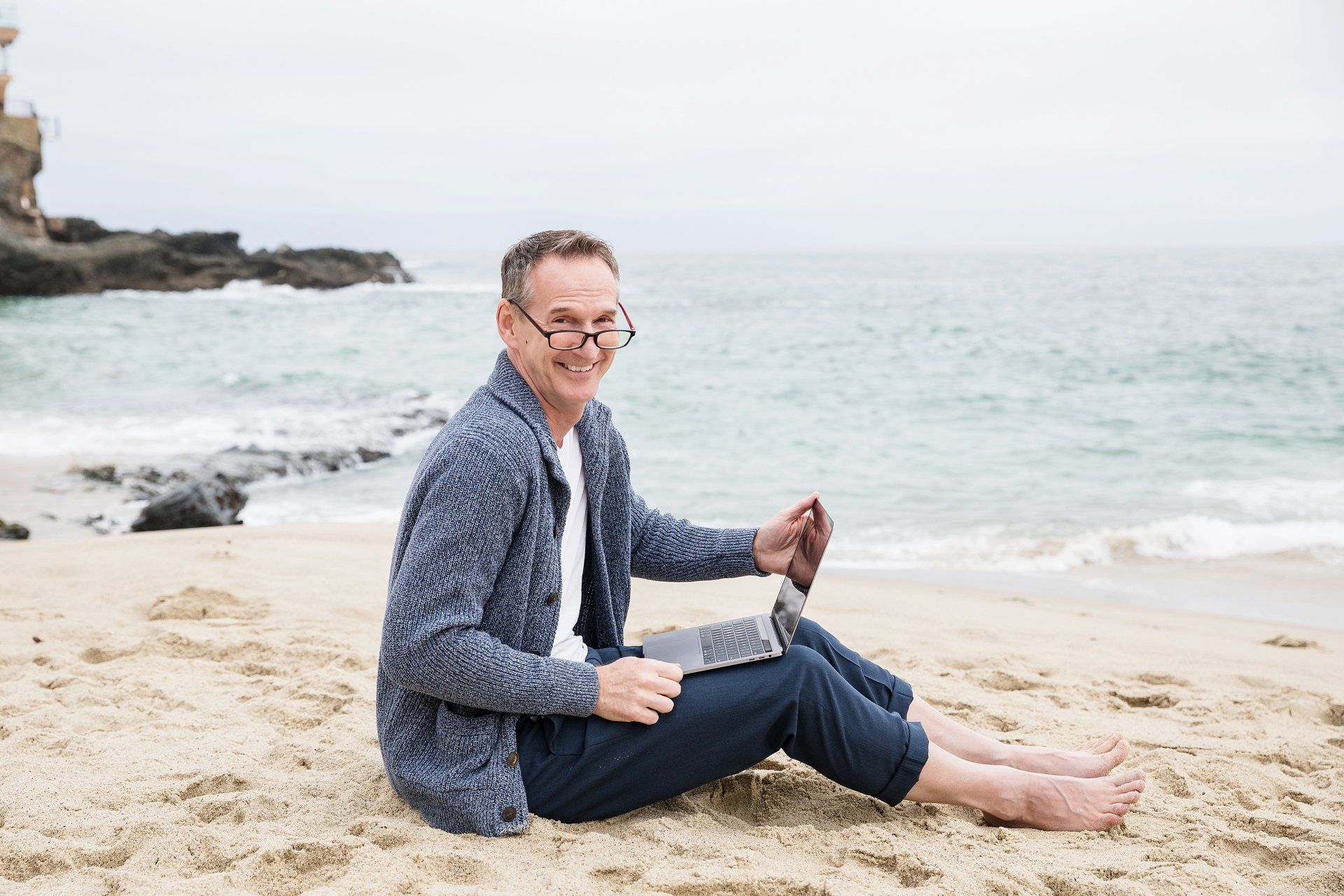 A man is sitting on the beach using a laptop.