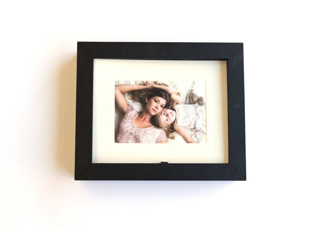 A picture of two women laying on a bed in a black frame.