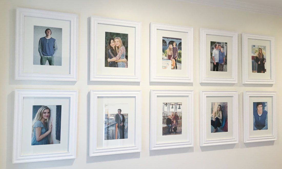 A bunch of pictures are hanging on a wall in white frames.