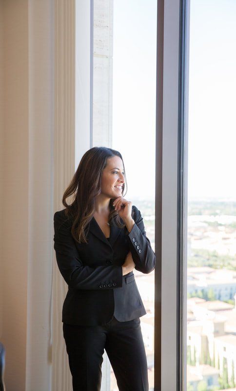 A woman in a suit is standing in front of a window looking out.