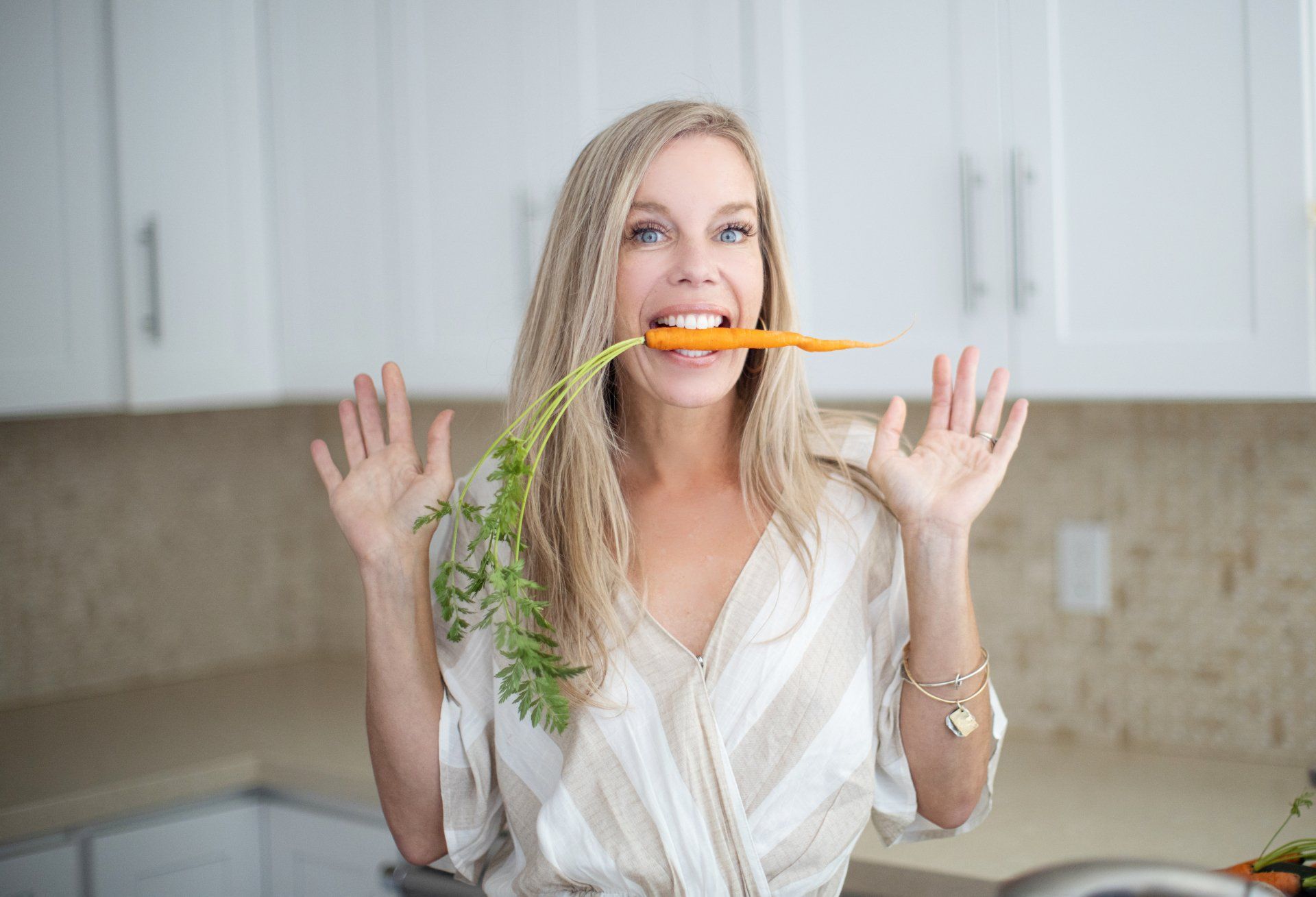 A woman is eating a carrot in a kitchen.