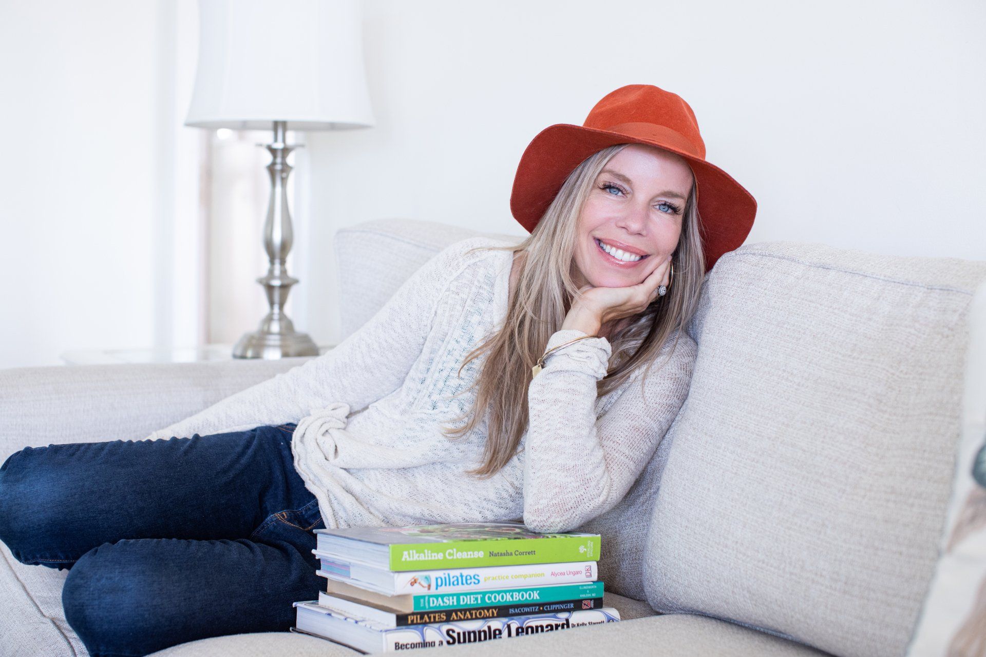 A woman is sitting on a couch with a stack of books.