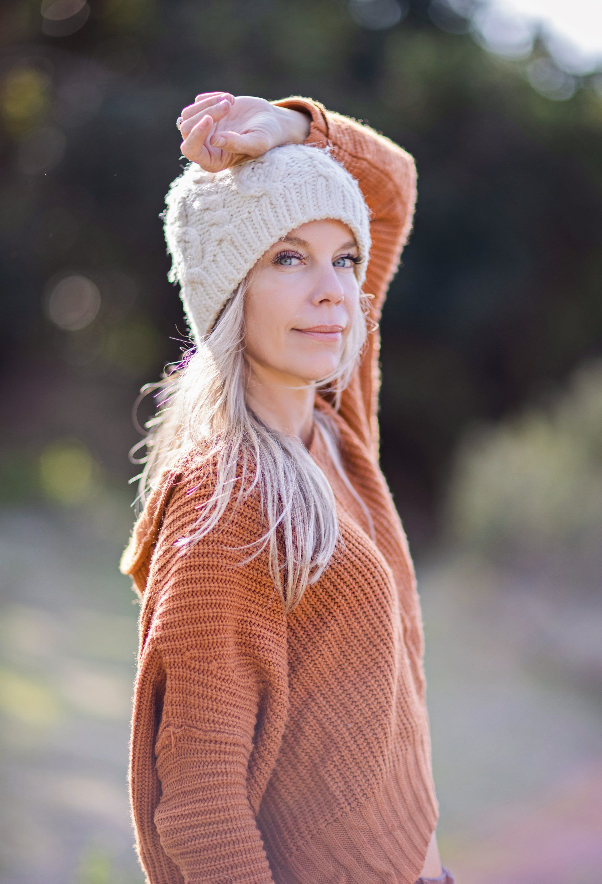 A woman wearing a sweater and a hat is standing in a field.