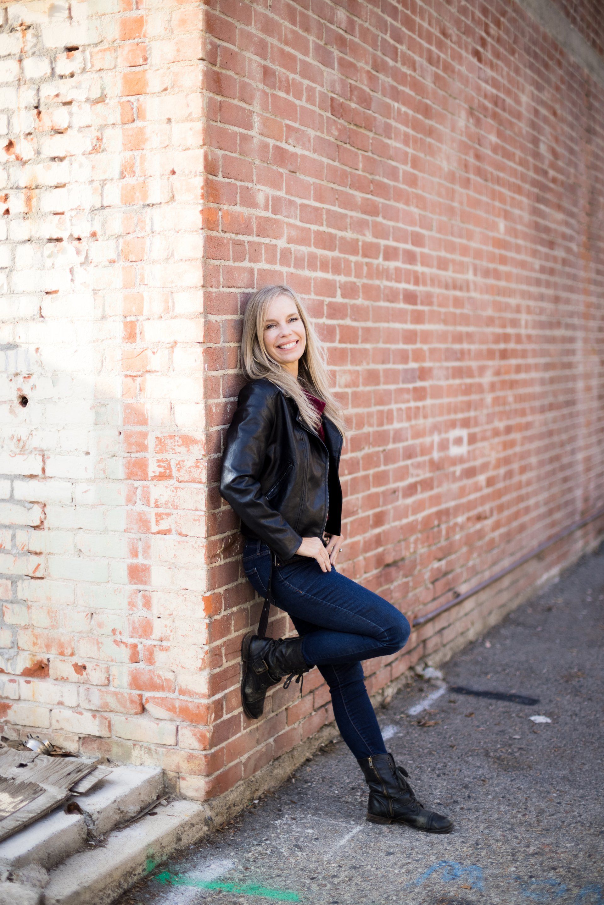 A woman is leaning against a brick wall in an alleyway.