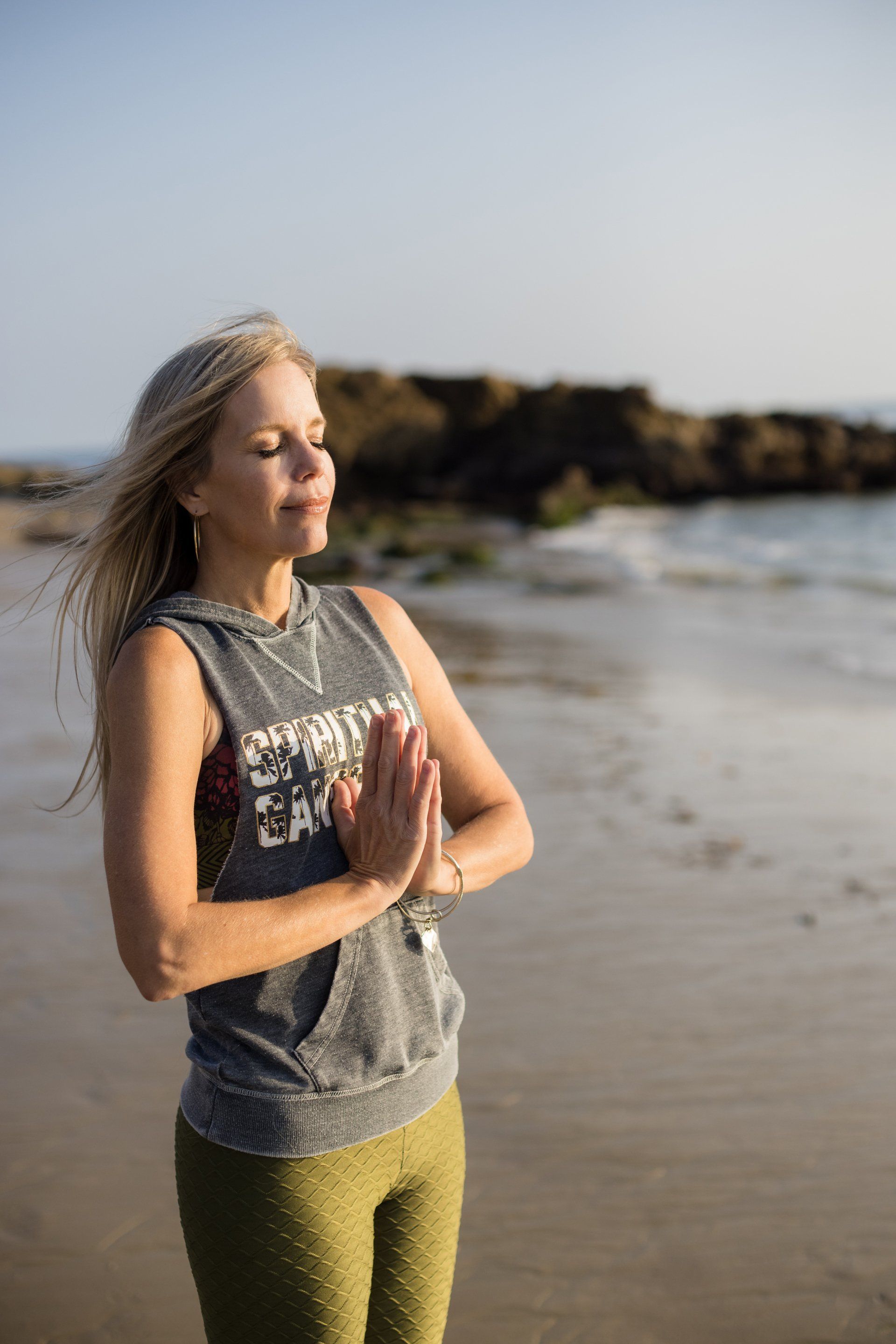 A woman is standing on a beach with her hands folded in prayer.
