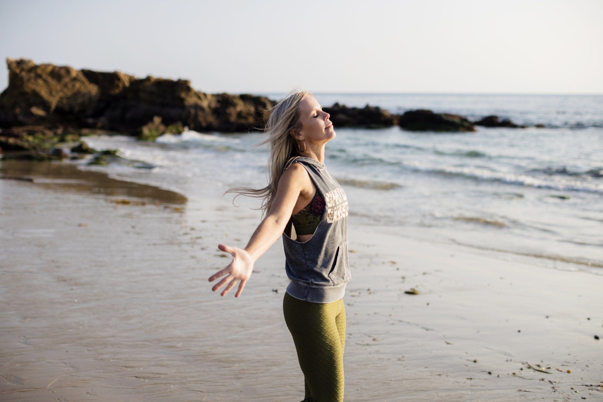 A woman is standing on a beach with her arms outstretched.