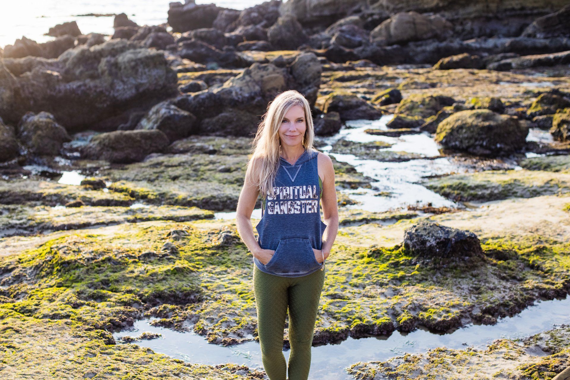 A woman in a blue tank top is standing on a rocky beach.