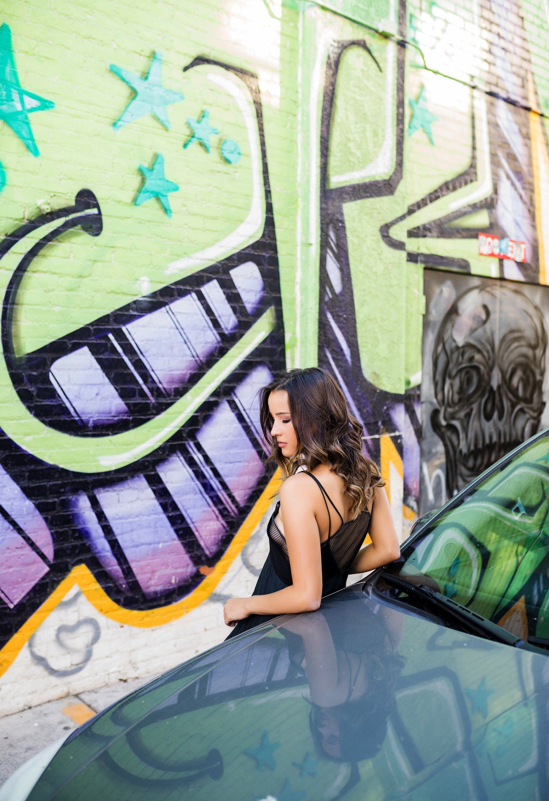 A woman is standing next to a car in front of a wall with graffiti on it.