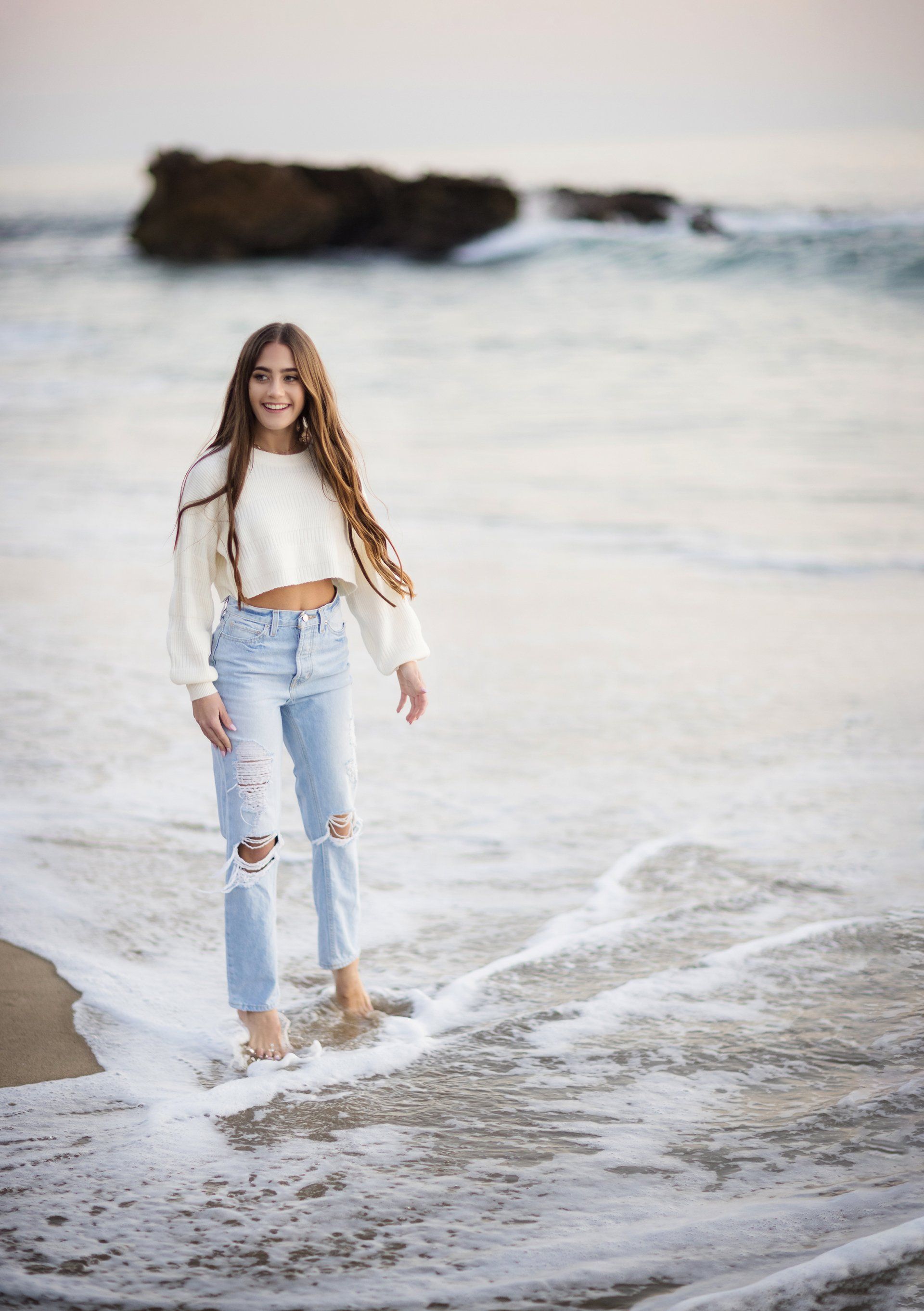 A woman is standing in the water on the beach.