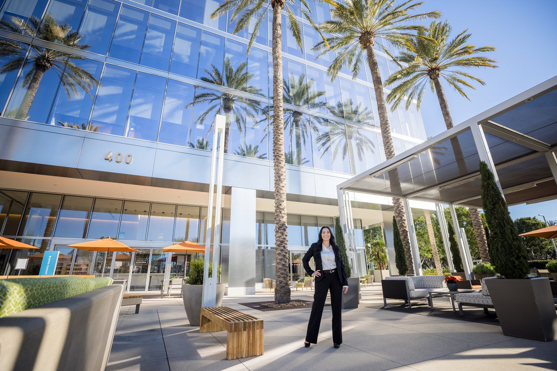 A woman in a suit is standing in front of a building with palm trees.