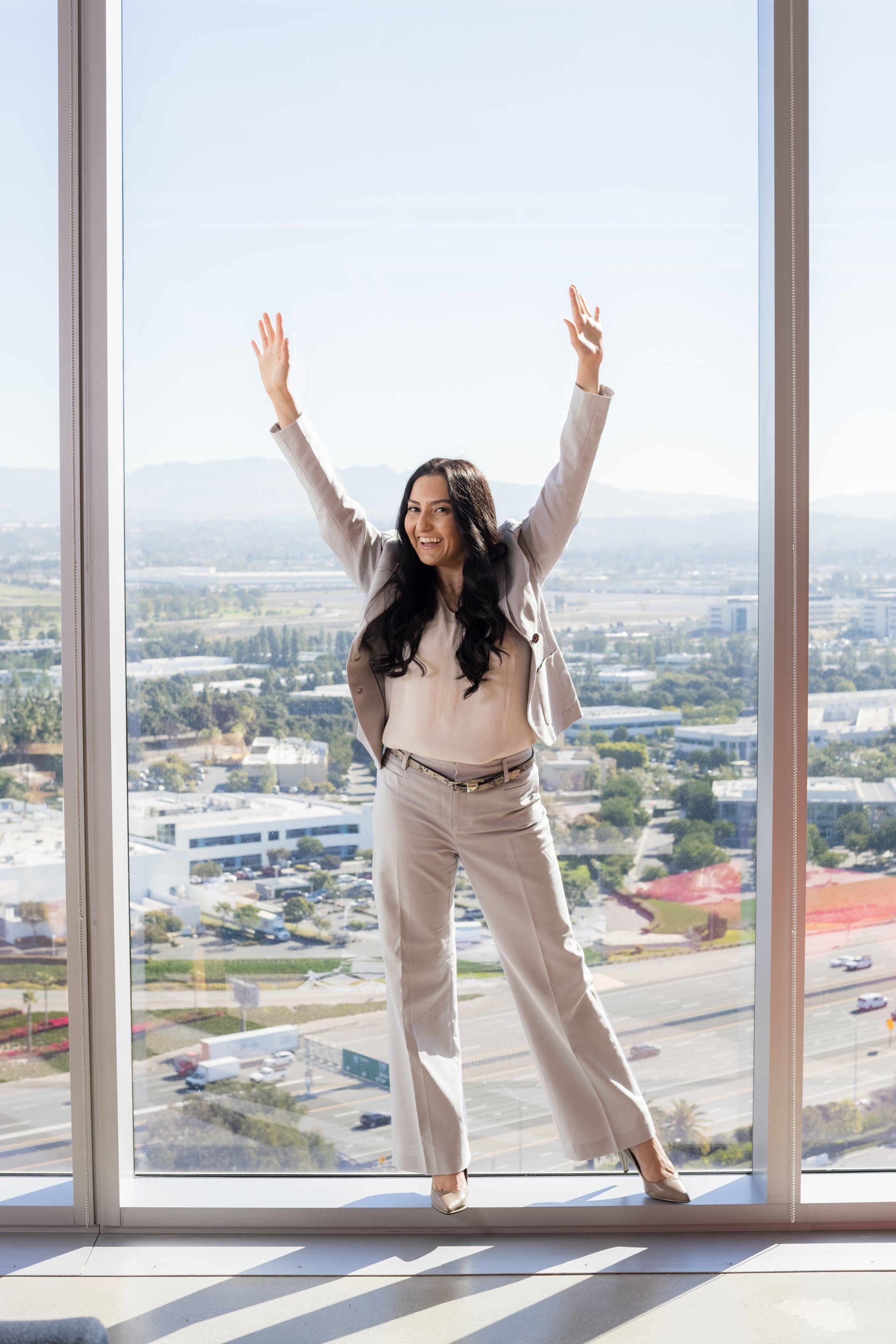 A woman in a suit is standing in front of a large window with her arms in the air.