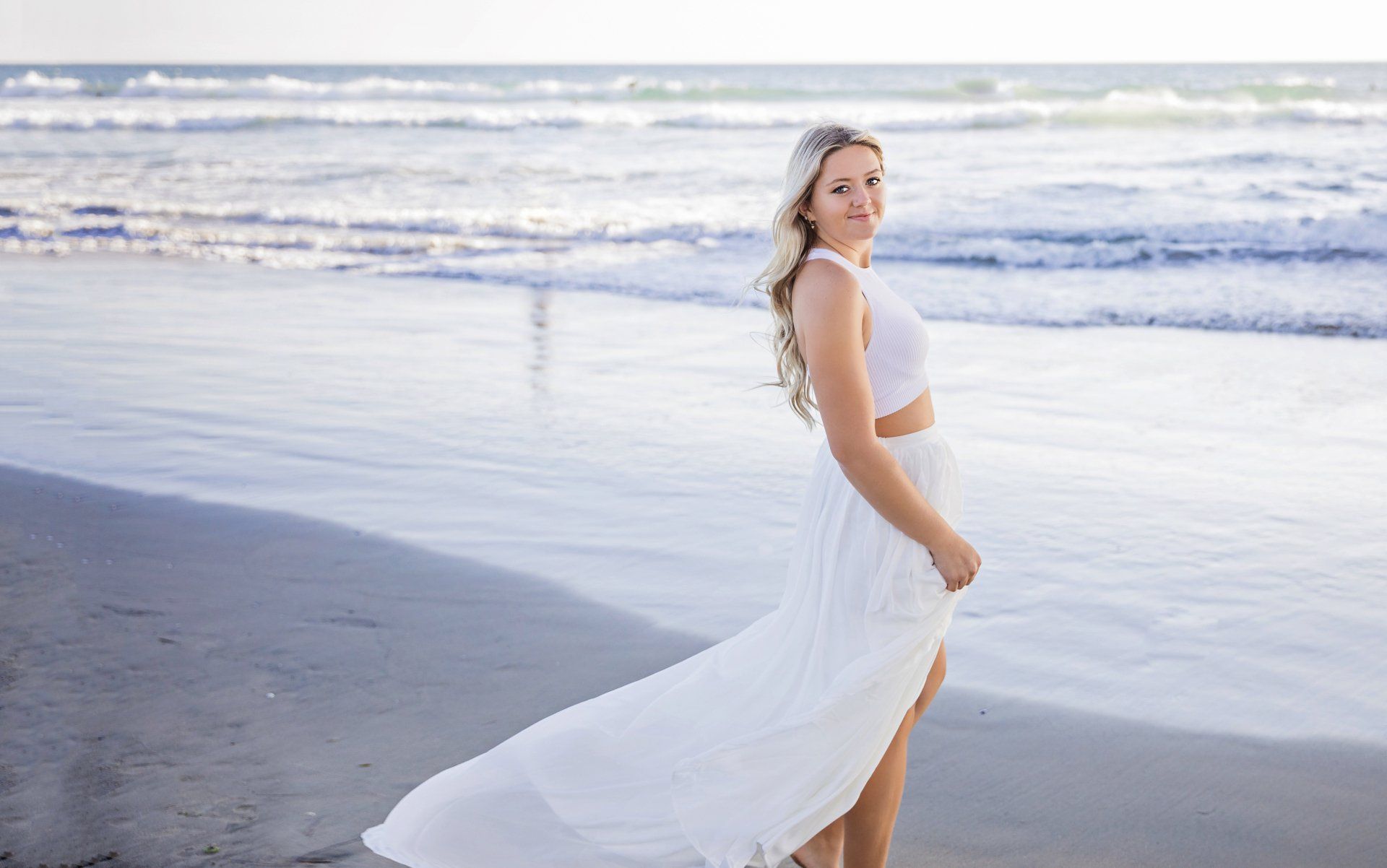 A woman in a white dress is standing on the beach.