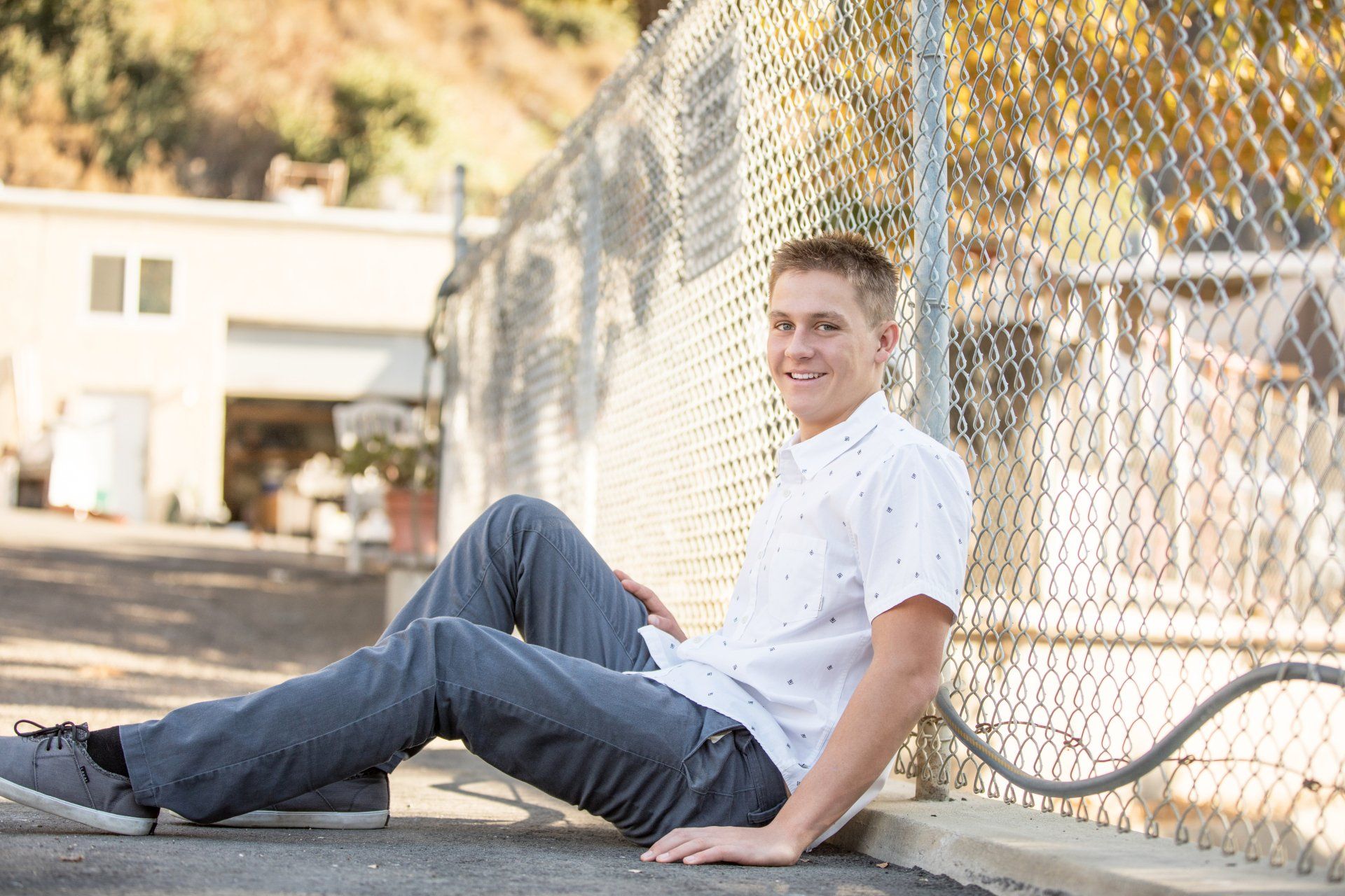 A young man is sitting on the ground next to a chain link fence.