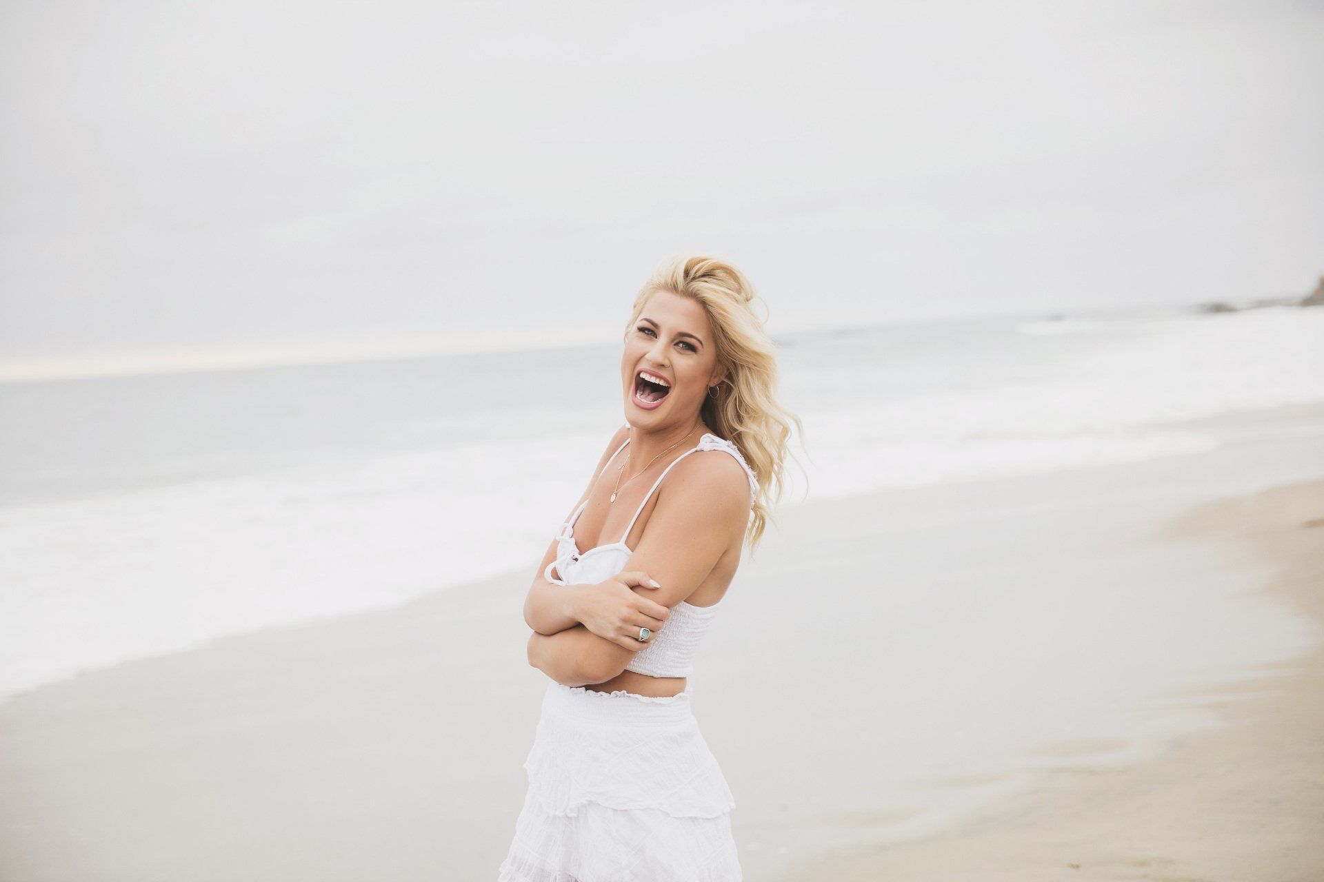 A woman in a white dress is laughing on the beach.