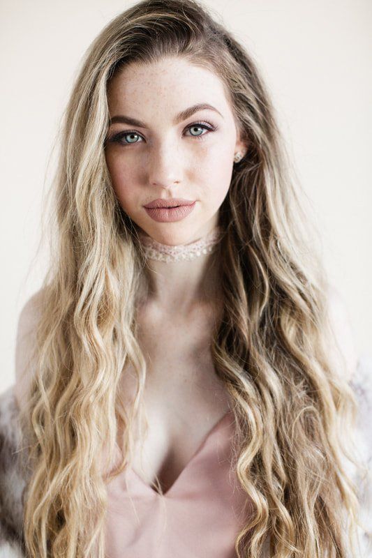 A woman with long blonde hair is wearing a choker and a pink top.