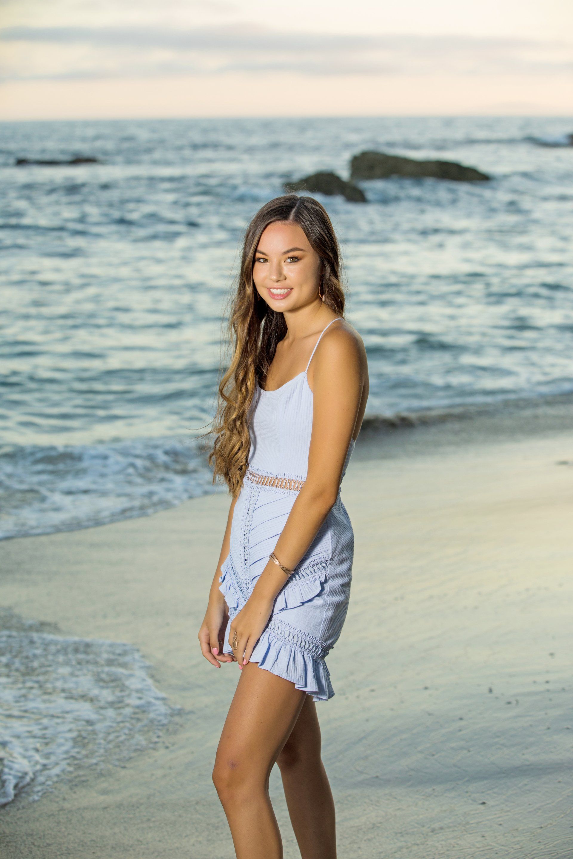 A young woman in a white dress is standing on a beach.