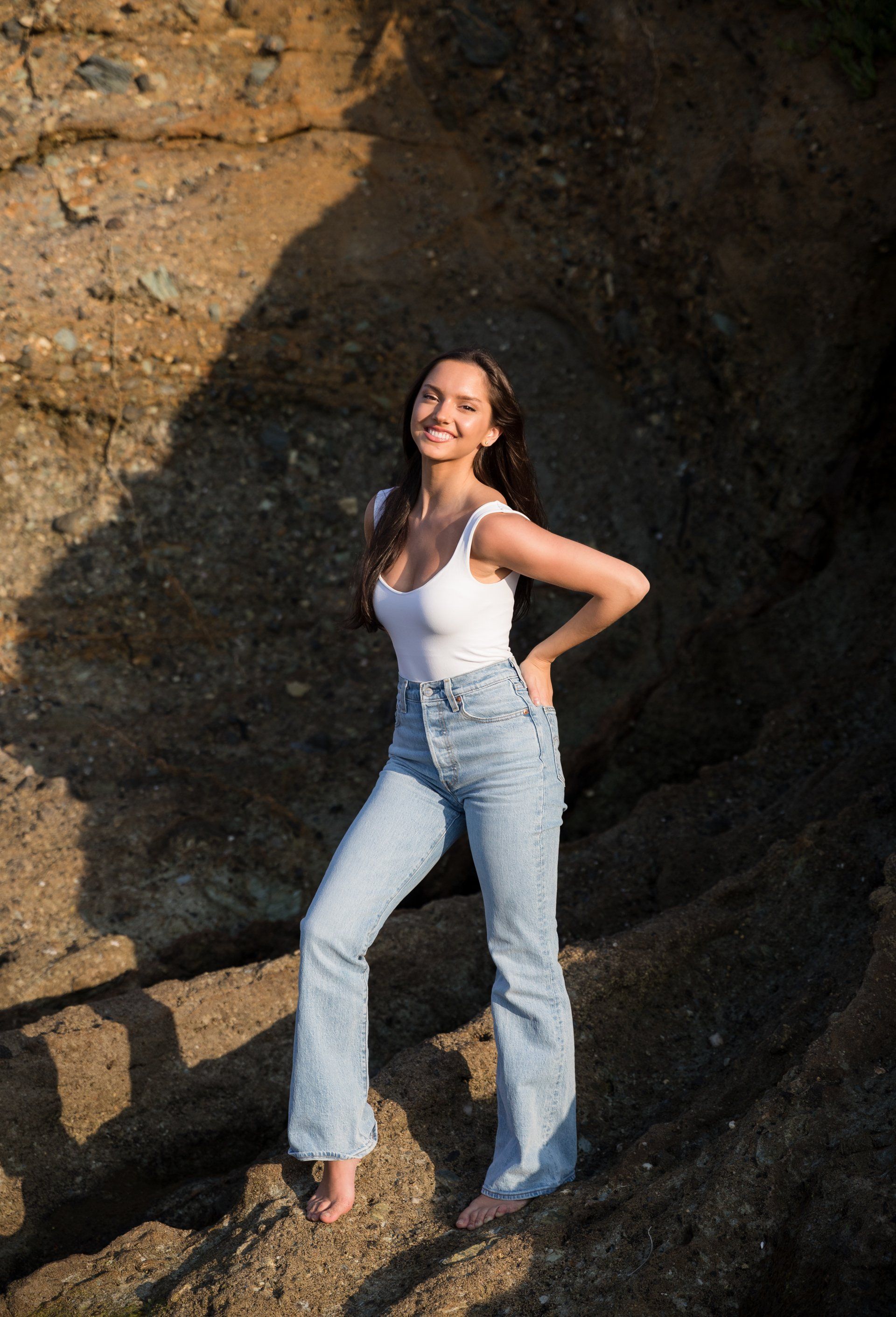 A woman in a white tank top and jeans is standing on a rock.