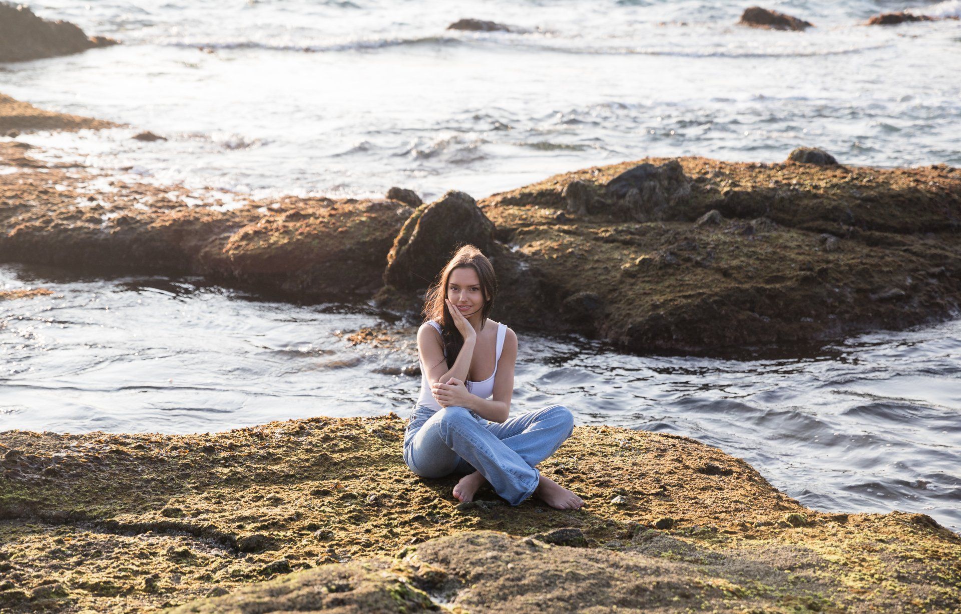 A woman is sitting on a rock near the ocean.