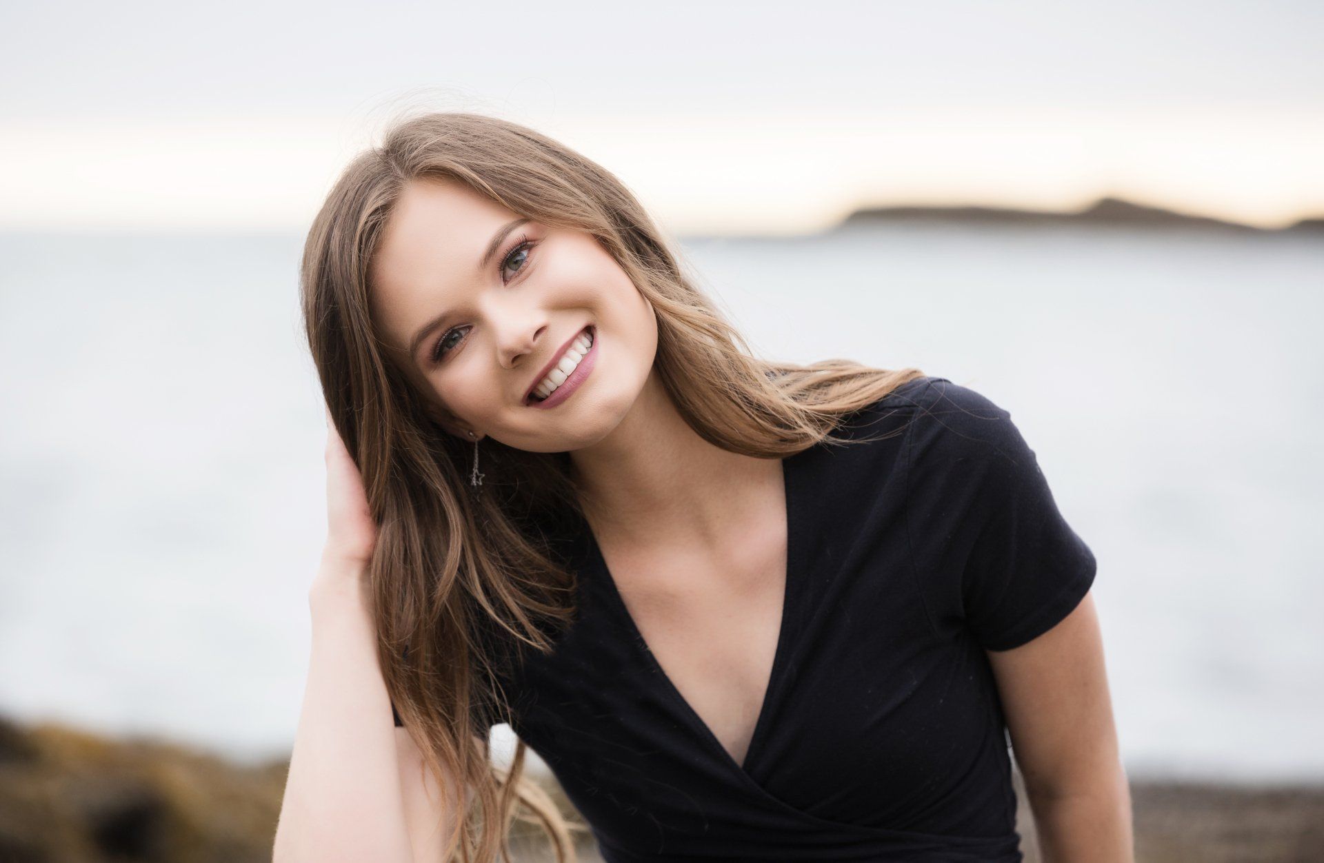 A woman in a black shirt is smiling and holding her hair.