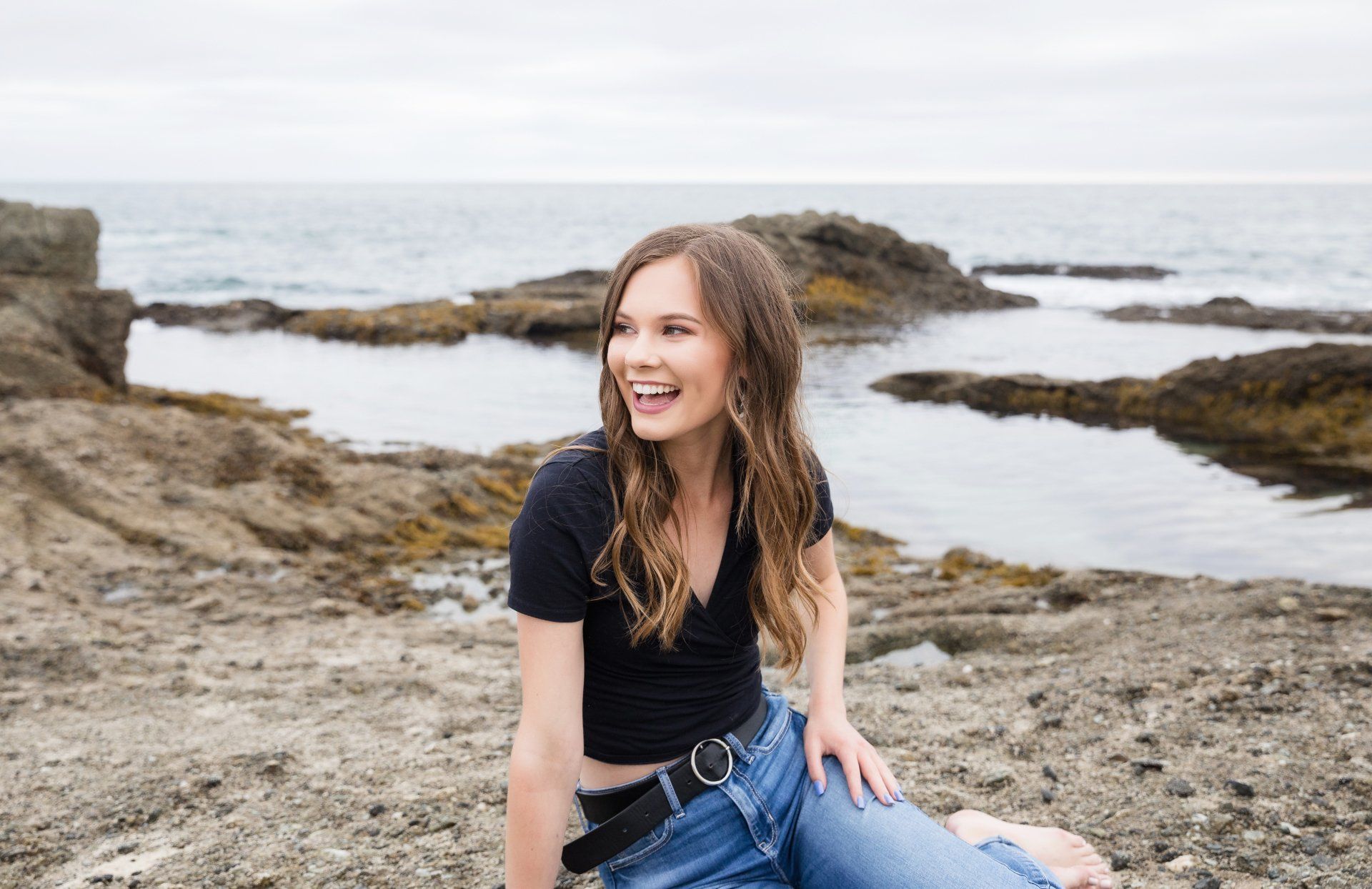 A woman is sitting on a rocky beach near the ocean.