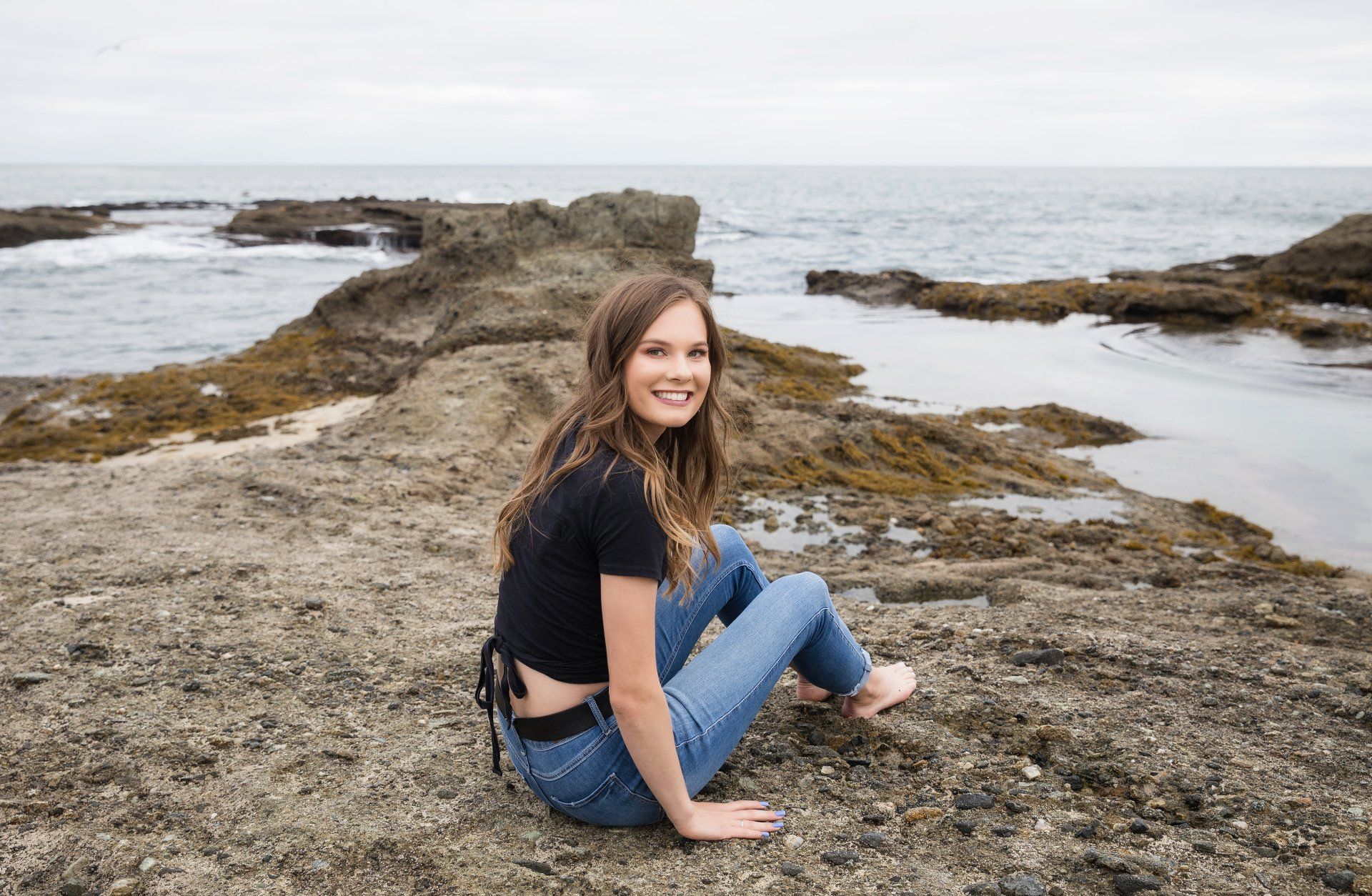 A woman is sitting on a rock near the ocean.