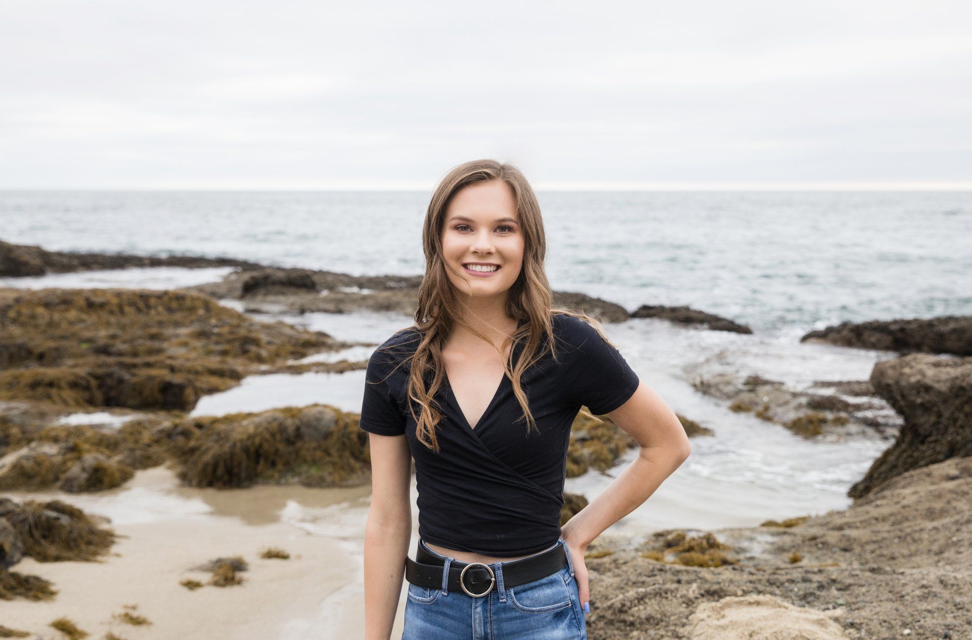 A young woman is standing on a rocky beach near the ocean.
