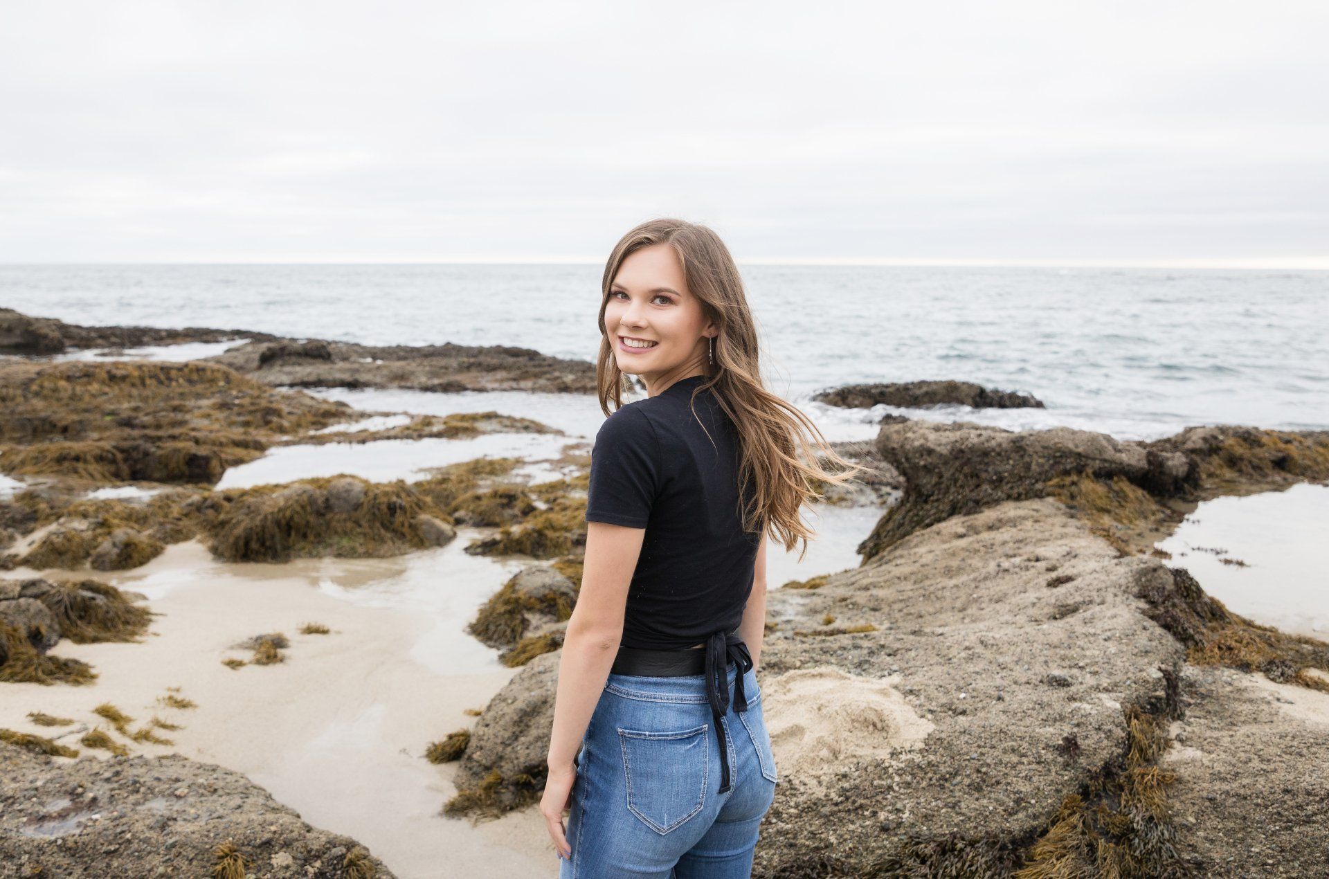 A woman is standing on a rocky beach near the ocean.