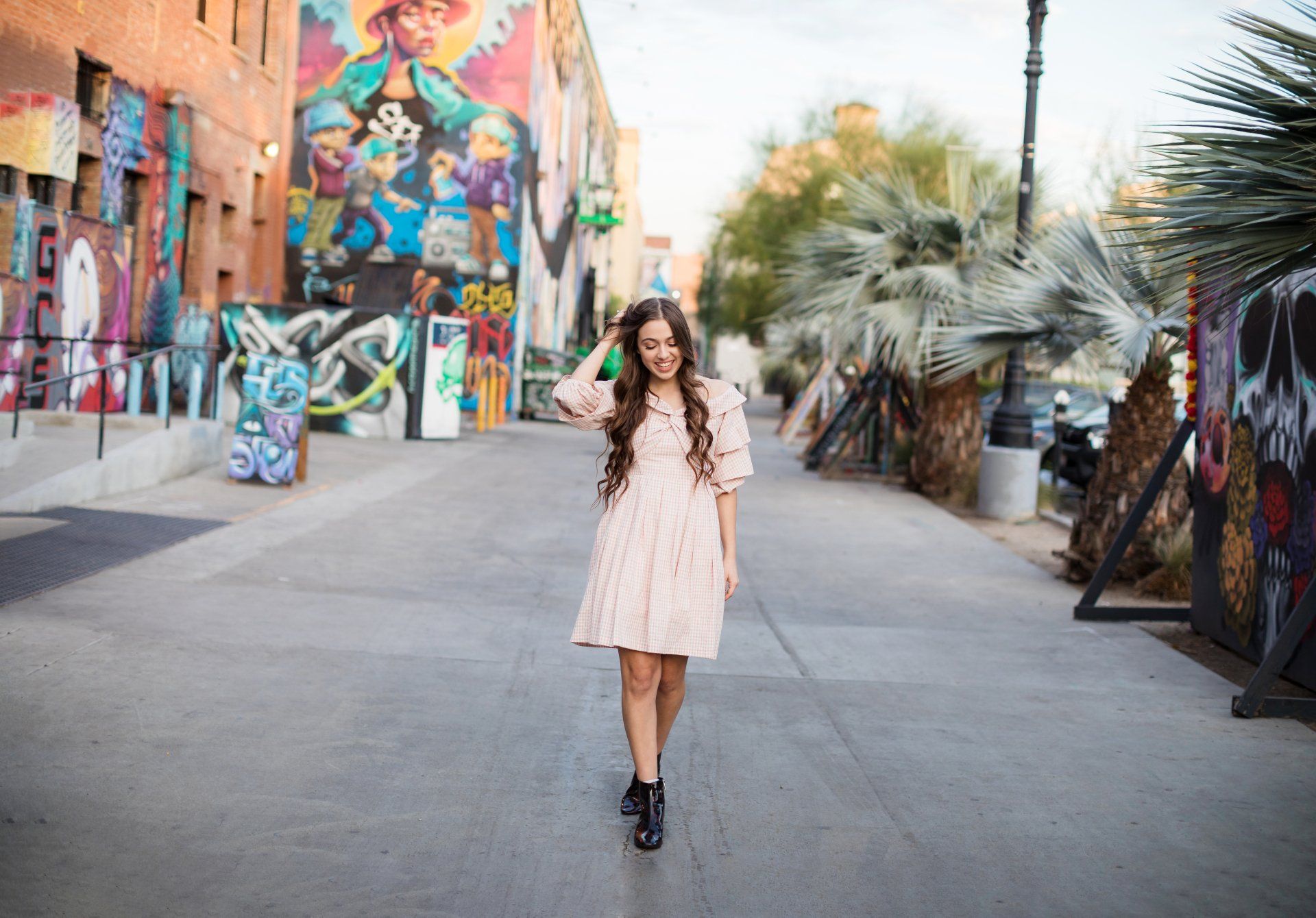 A woman in a pink dress is walking down a street in front of a mural.