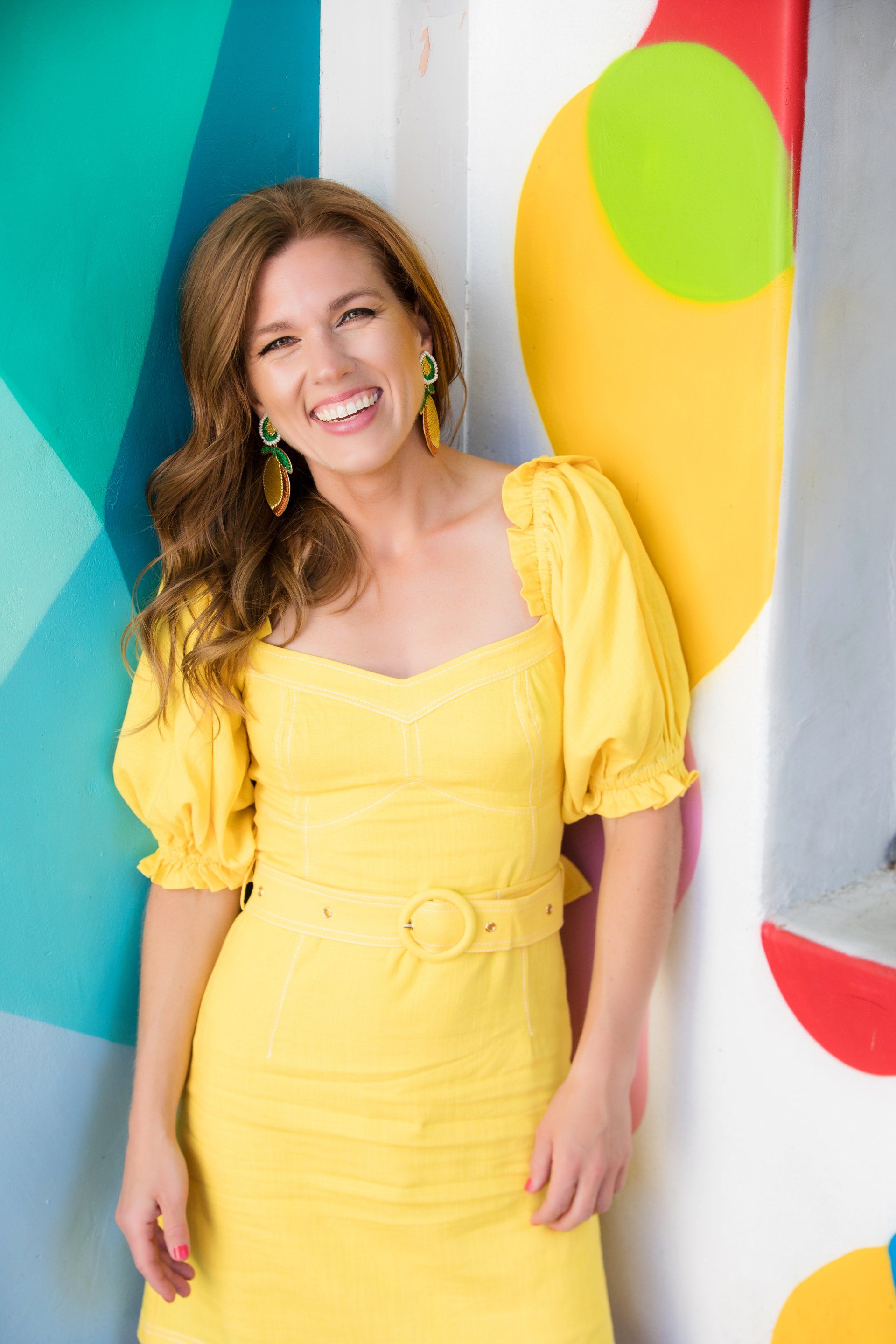 A woman in a yellow dress is standing in front of a colorful wall.