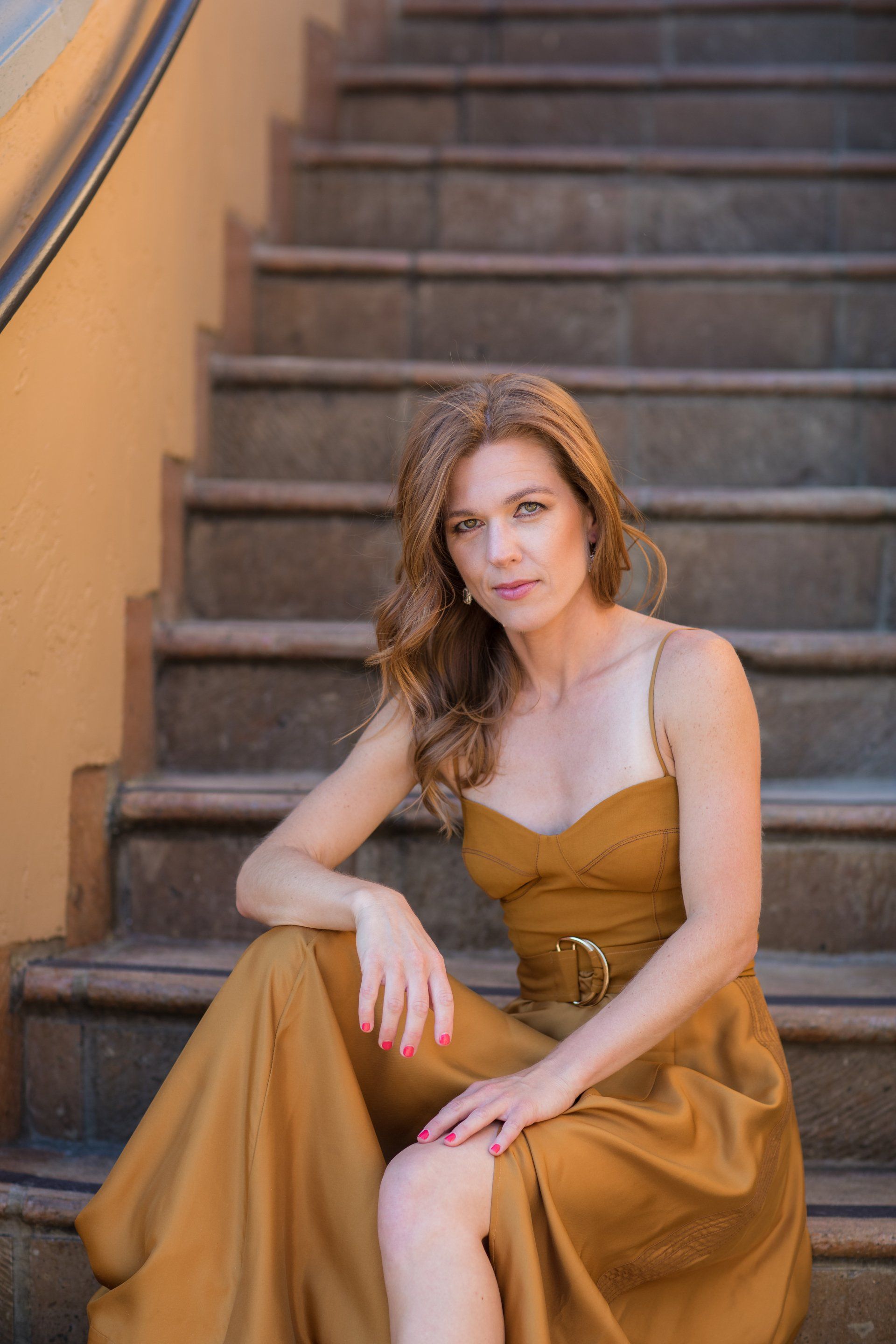 A woman in a long gold dress is sitting on a set of stairs.