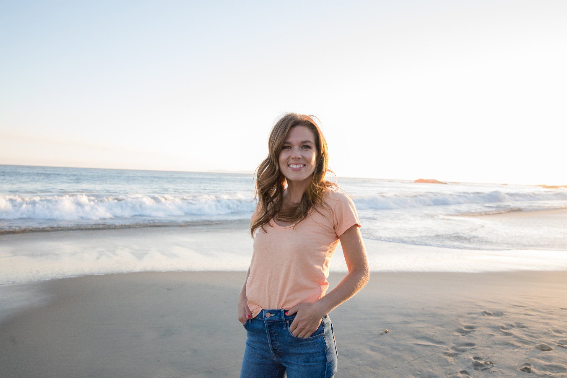 A woman is standing on a beach with her hands in her pockets.