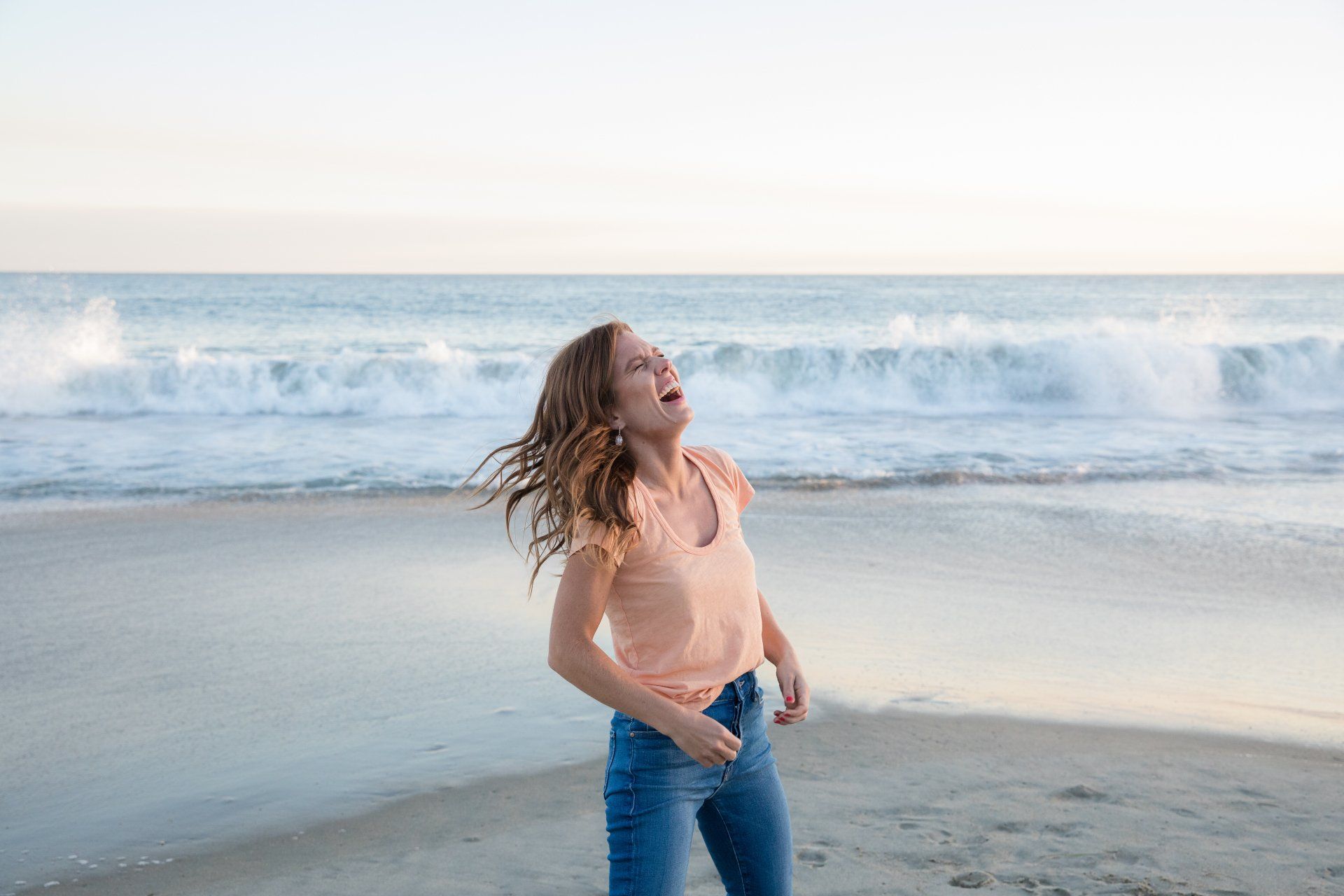 A young woman is standing on a beach with her arms outstretched.