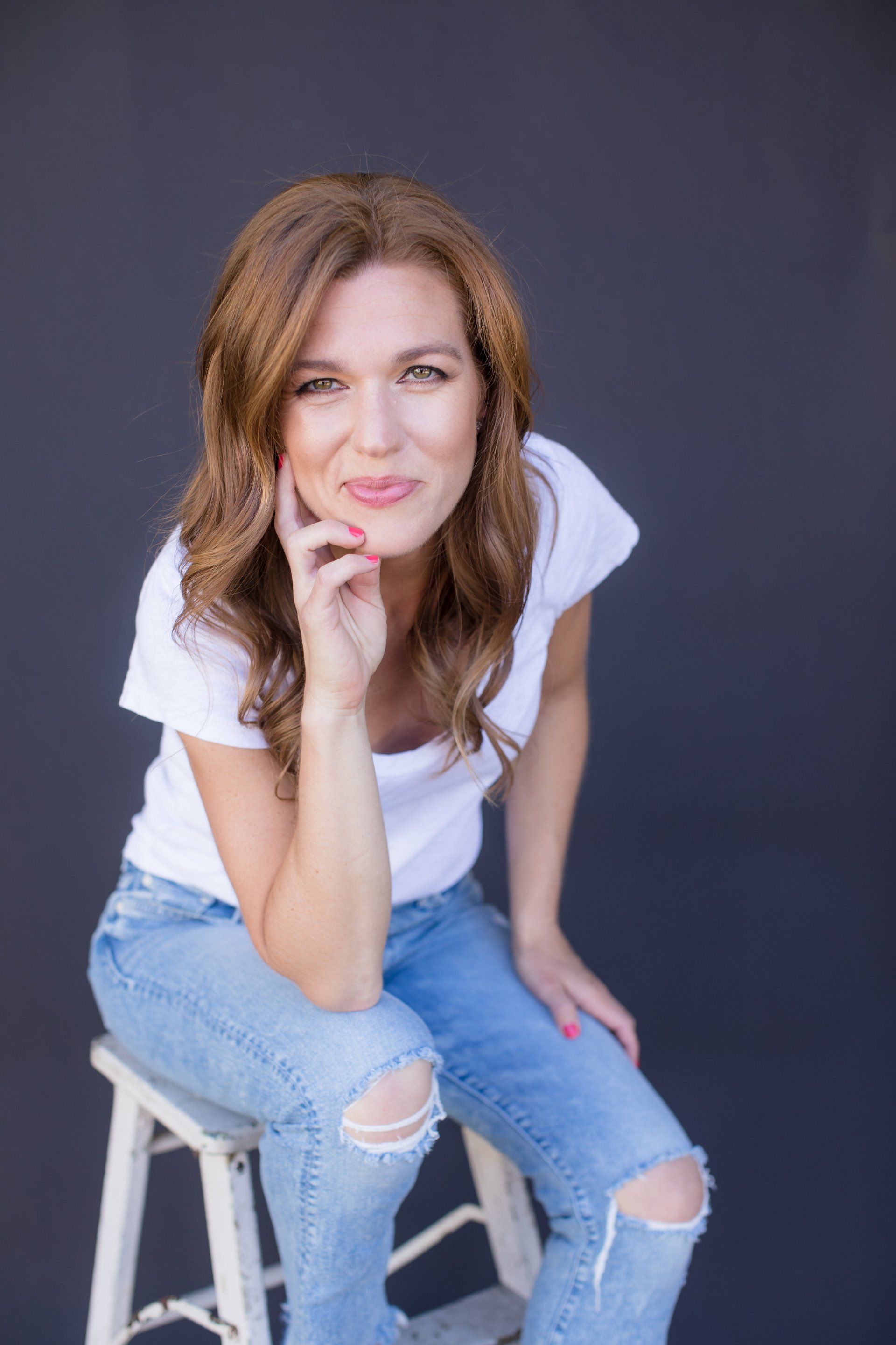 A woman is sitting on a stool with her hand on her chin.