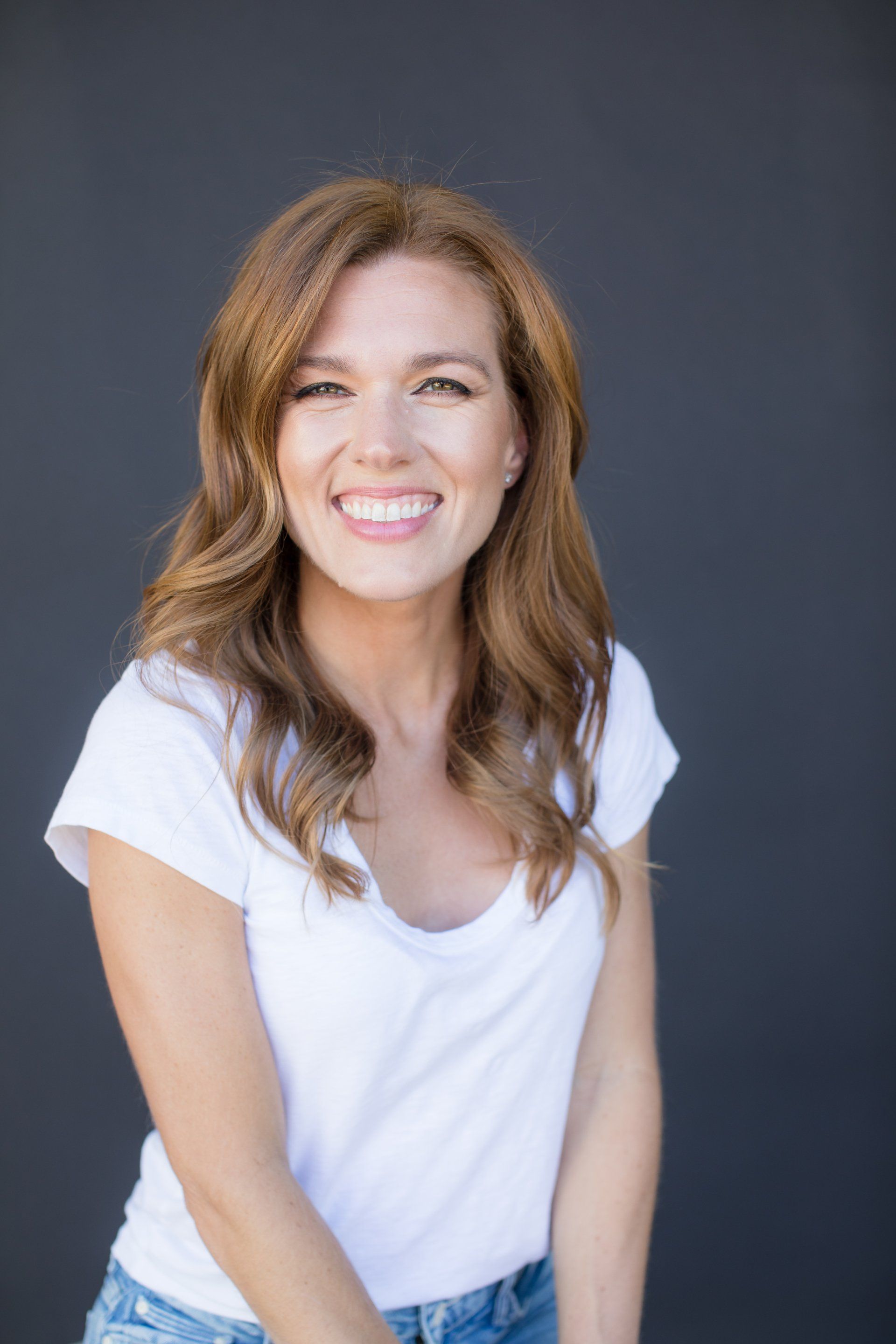 A woman in a white t-shirt and jeans is smiling for the camera.