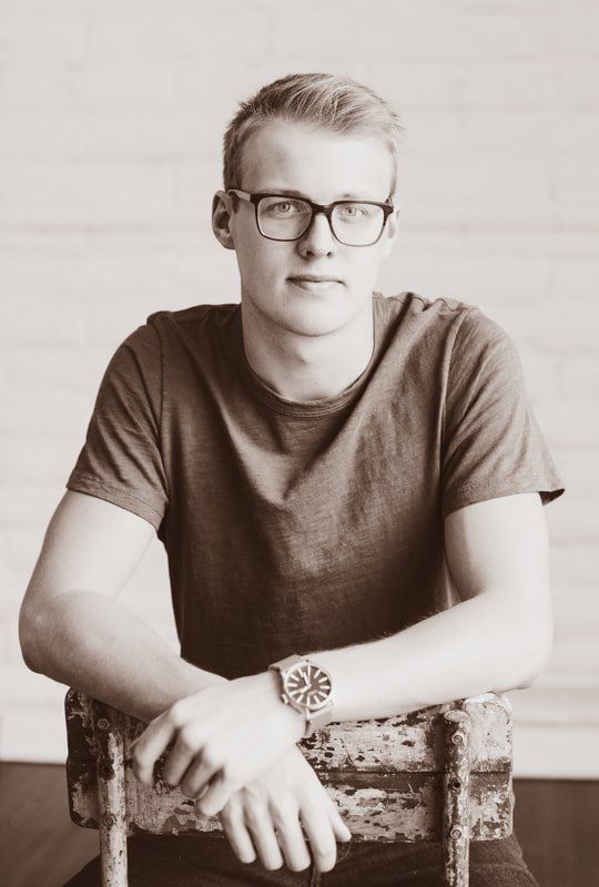 A young man wearing glasses and a watch is sitting in a chair.