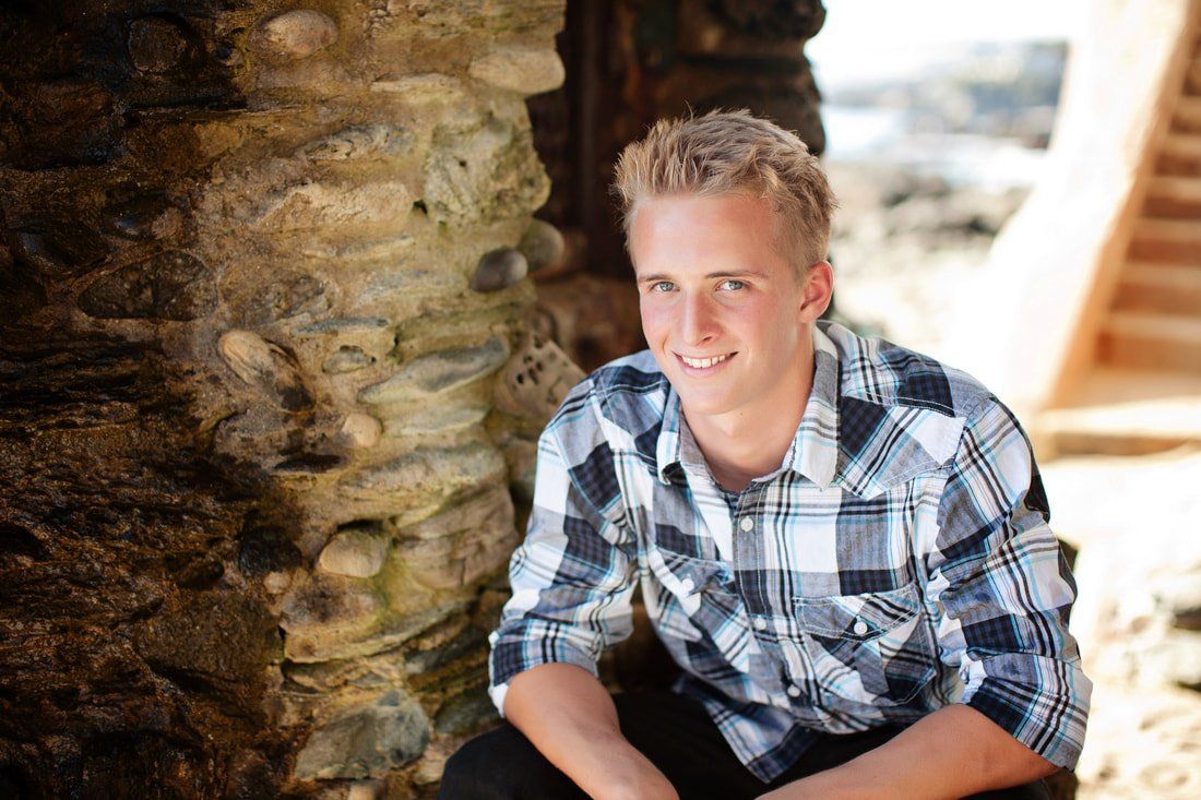 A young man in a plaid shirt is sitting next to a stone wall.