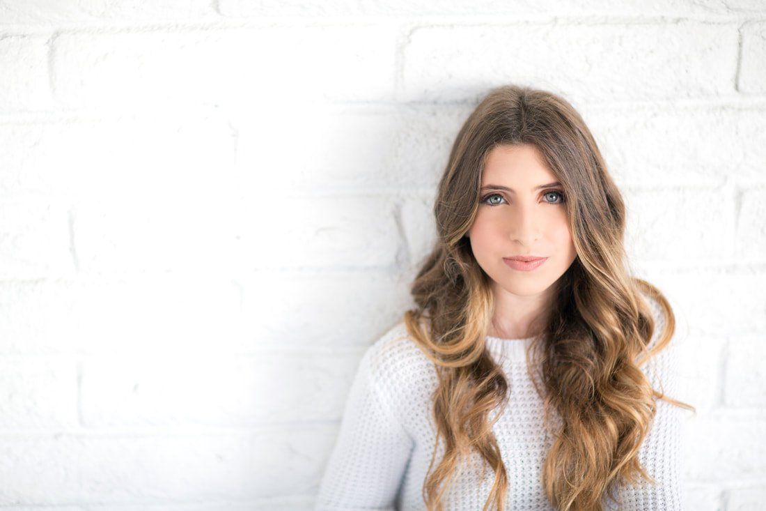 A woman with long hair is standing in front of a white brick wall.