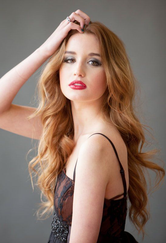 A woman with long red hair is wearing a black dress and red lipstick.