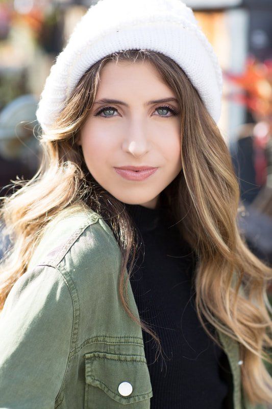 A woman wearing a white hat and a green jacket is looking at the camera.