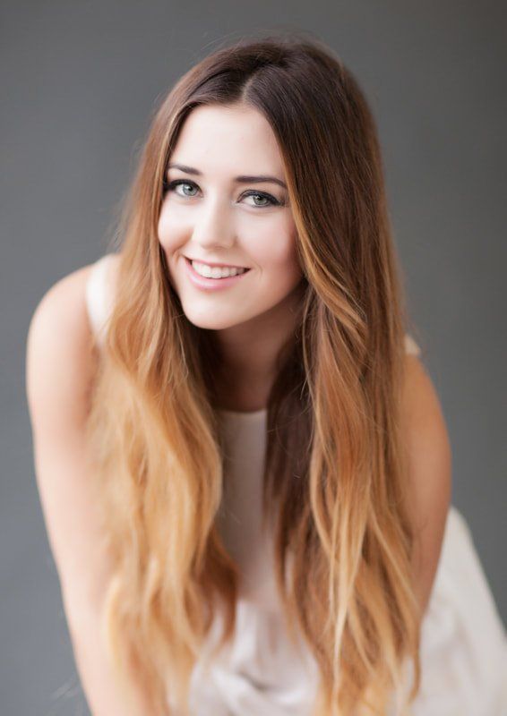A woman with long hair is wearing a white dress and smiling.